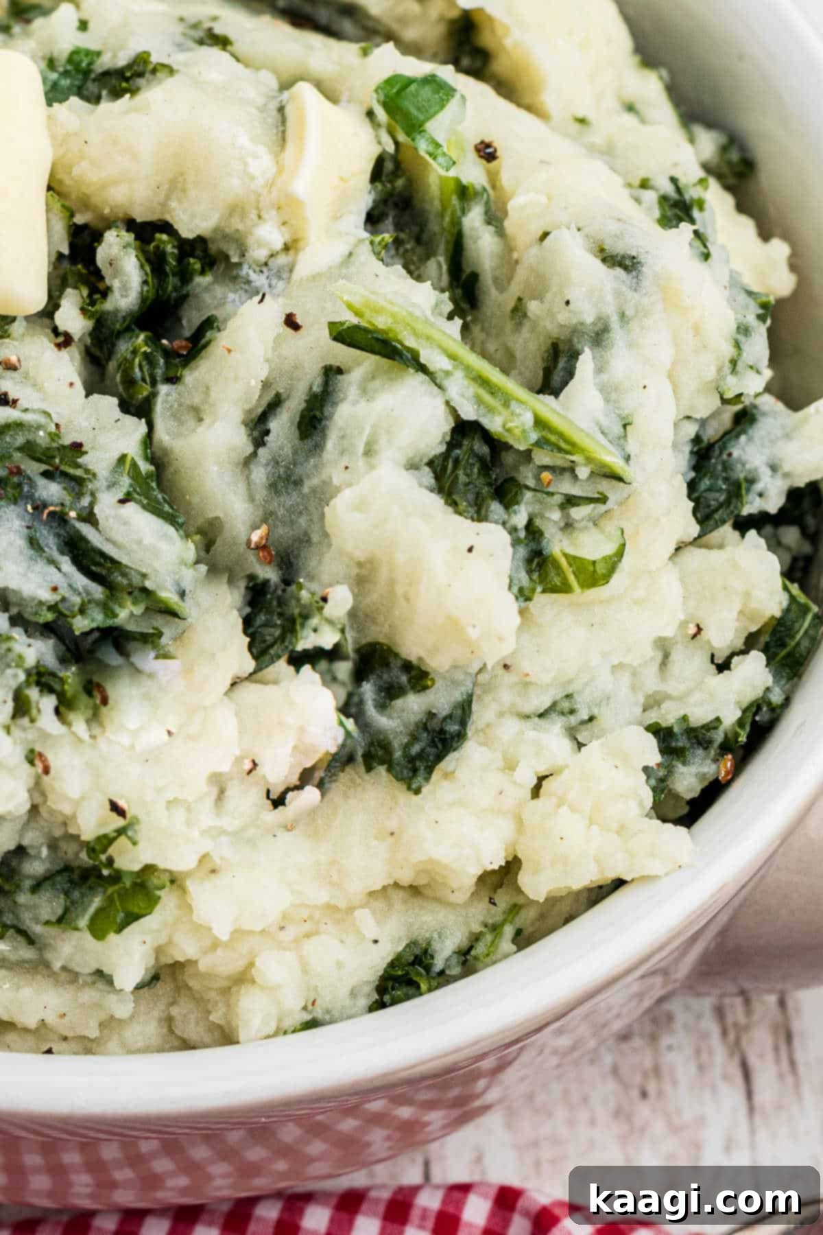 Very close up shot of a bowl of traditional colcannon, highlighting the tender kale mixed into creamy mashed potatoes, with a melting pat of butter.