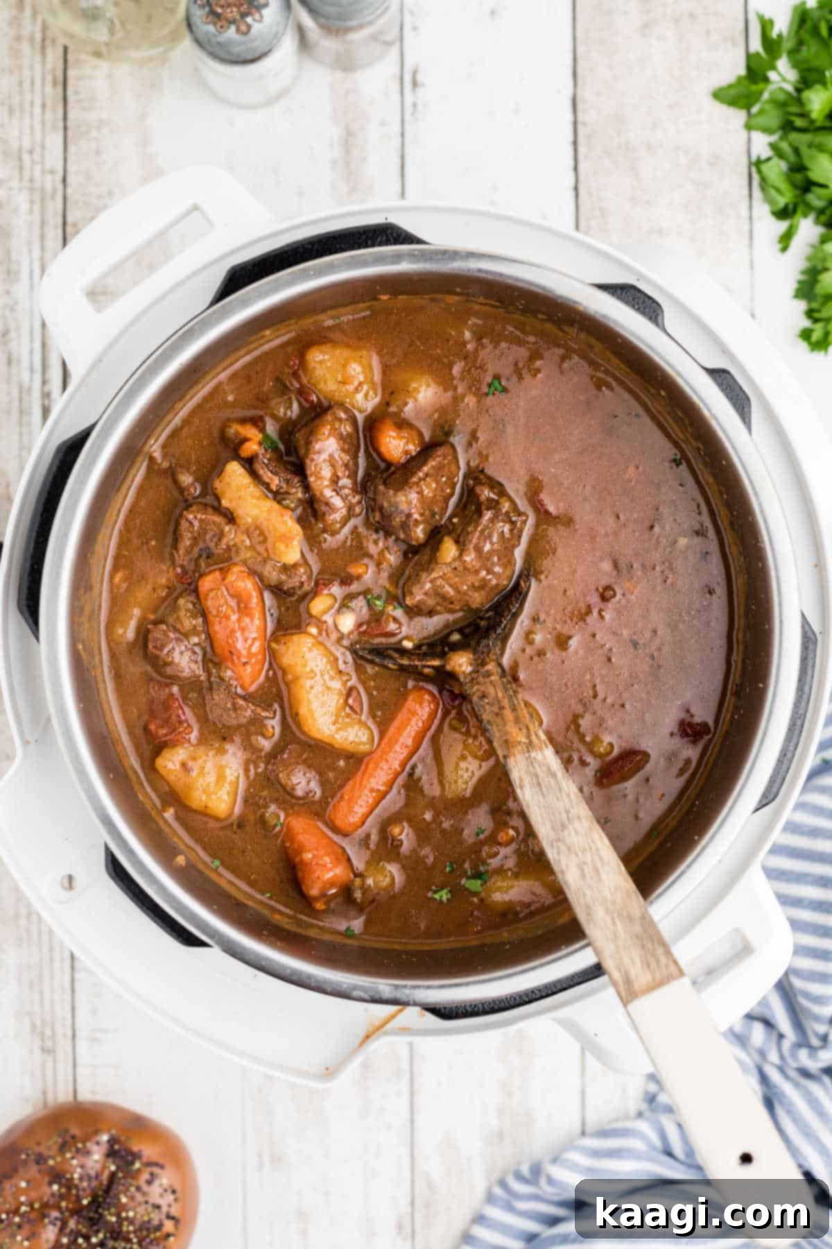 Overhead shot of an open instant pot with venison stew and a wooden spoon, showcasing the rich texture and chunks of meat and vegetables.