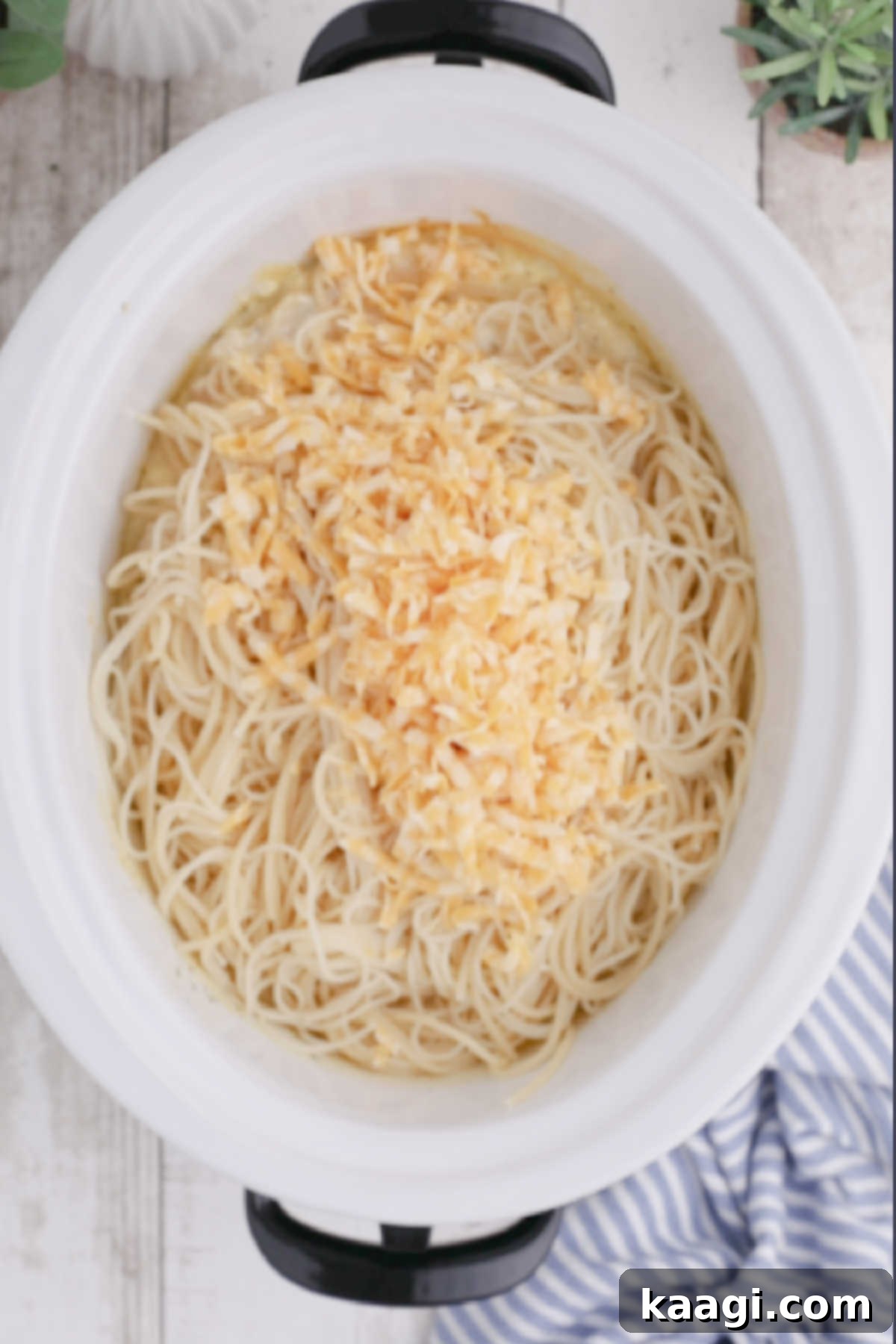 Creamy Slow Cooker Ranch Chicken Spaghetti 11 Spaghetti noodles and grated cheese are visibly mixed into a slow cooker, suggesting the final stages of the recipe.