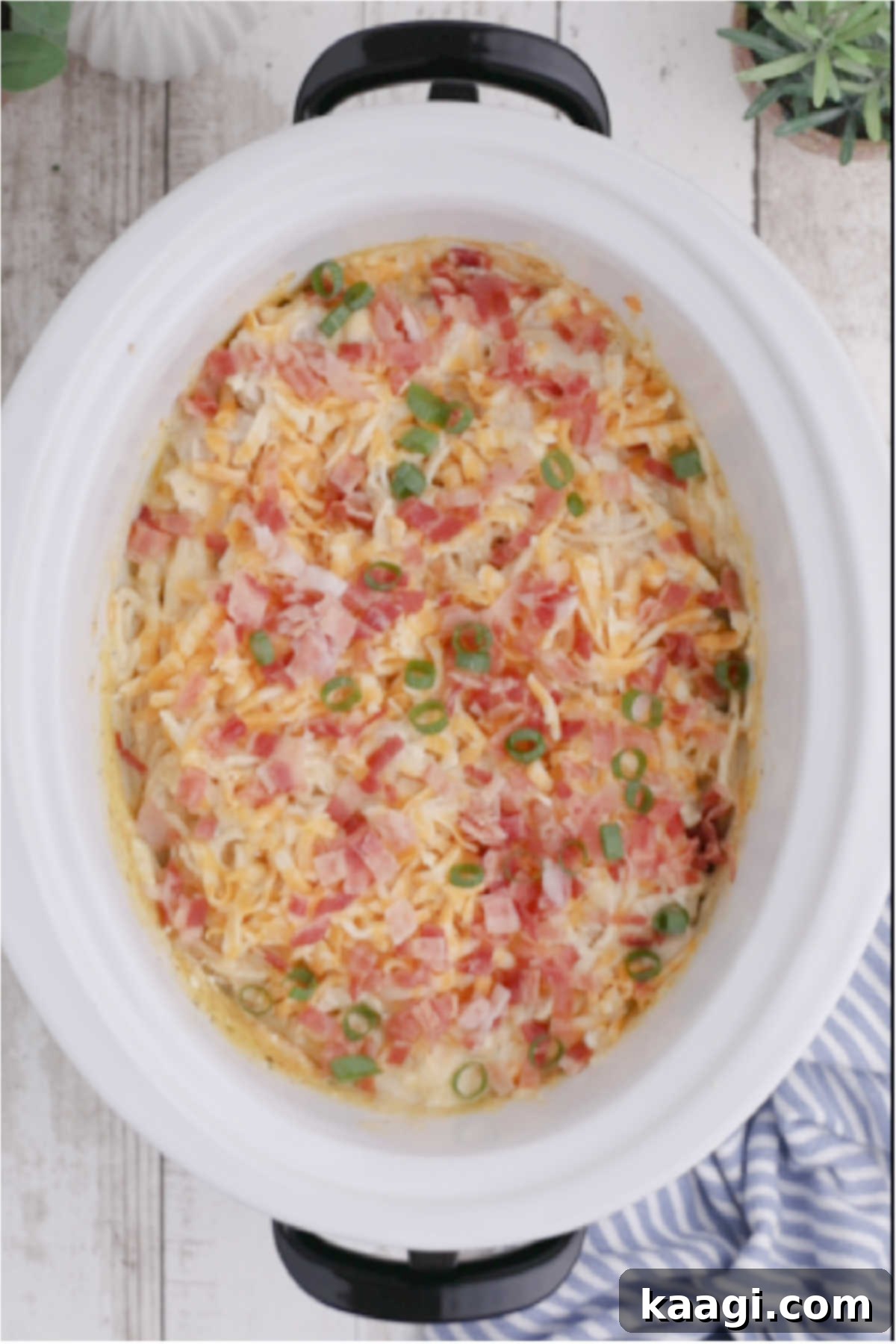 Creamy Slow Cooker Ranch Chicken Spaghetti 12 A slow cooker filled with ranch chicken spaghetti, generously topped with melted cheese, crispy bacon bits, and freshly chopped green onions, ready to be served.
