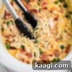 Creamy Slow Cooker Ranch Chicken Spaghetti 17 A pair of tongs digging into a creamy Crock Pot Ranch Chicken Spaghetti, ready for serving.