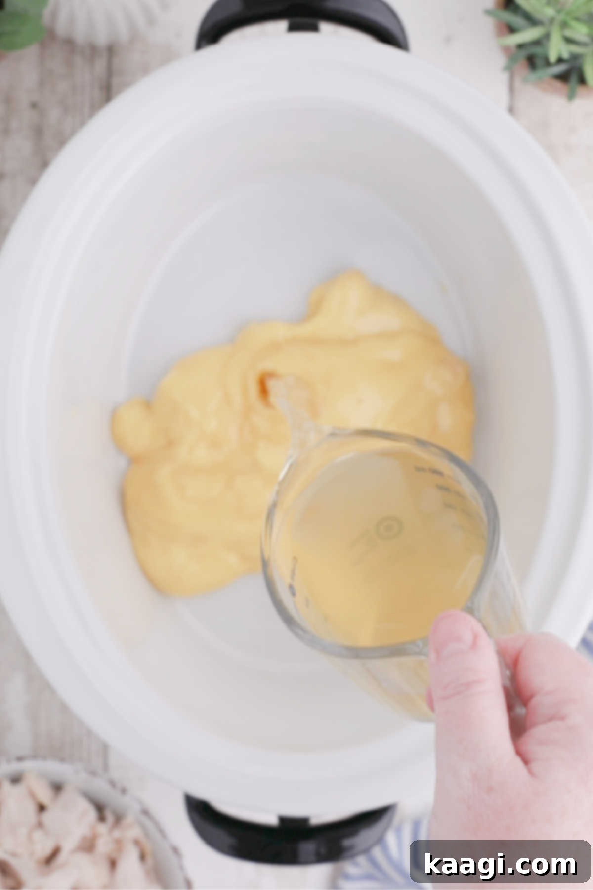 Creamy Slow Cooker Ranch Chicken Spaghetti 4 Chicken soup is being carefully added to a clean, white crock pot insert, ready for the slow cooking process.