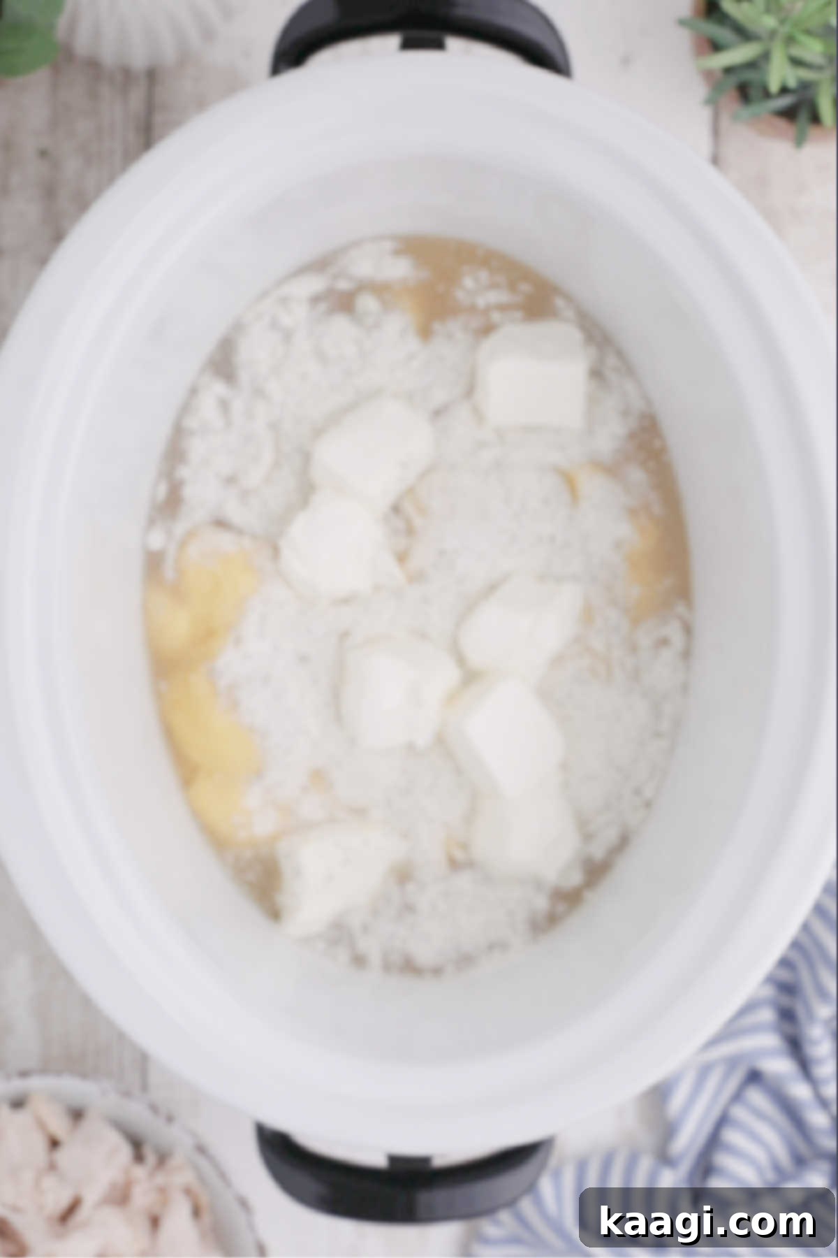 Creamy Slow Cooker Ranch Chicken Spaghetti 5 Small cubes of softened cream cheese are being gently placed into a crock pot, alongside other ingredients, for even melting.