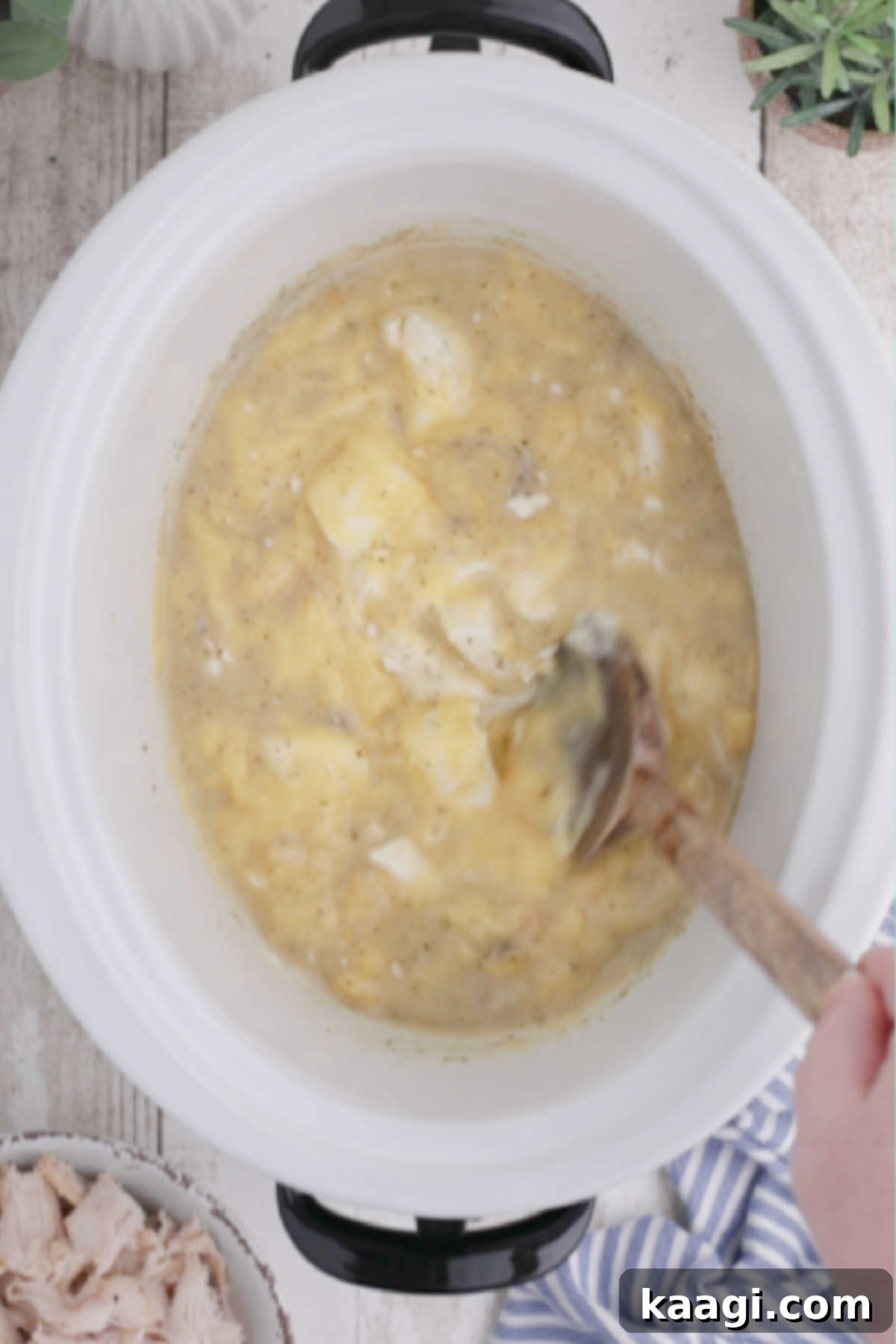 Creamy Slow Cooker Ranch Chicken Spaghetti 7 A wooden spoon actively stirring the melting ingredients inside a crock pot, ensuring a smooth and consistent sauce.