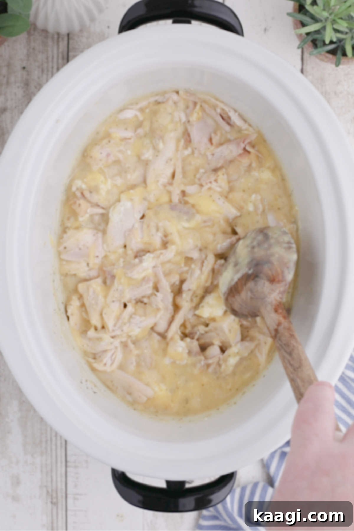 Creamy Slow Cooker Ranch Chicken Spaghetti 8 Shredded chicken is being added to the creamy sauce in a crock pot and stirred thoroughly to combine all the ingredients.