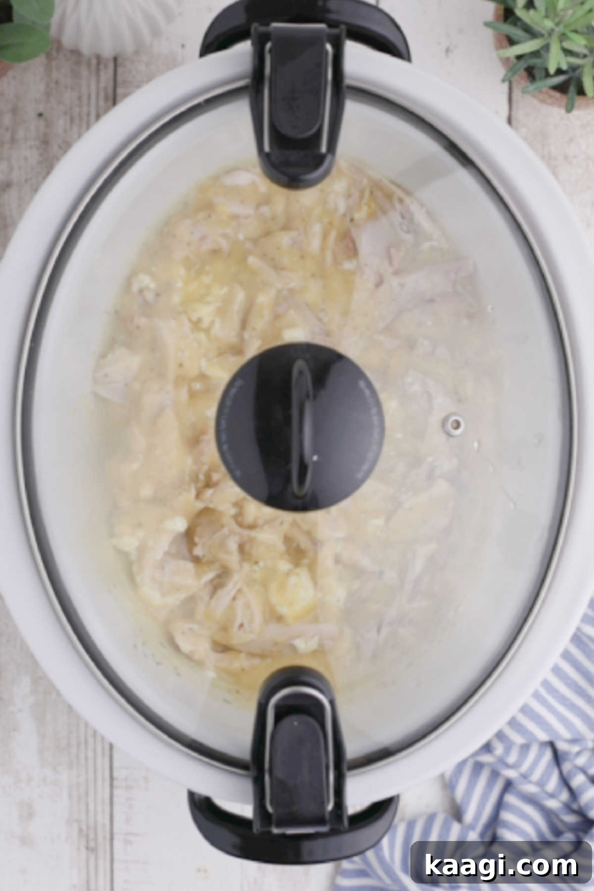 Creamy Slow Cooker Ranch Chicken Spaghetti 9 A slow cooker with its lid closed, simmering ingredients for a chicken spaghetti dish, indicating active cooking.