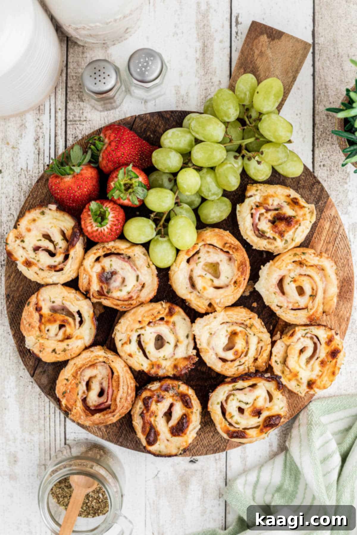 Overhead shot of a board full of ham and cheese bites with some fruit.