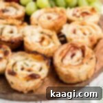 A board with ham and cheese bites with some grapes in the background.