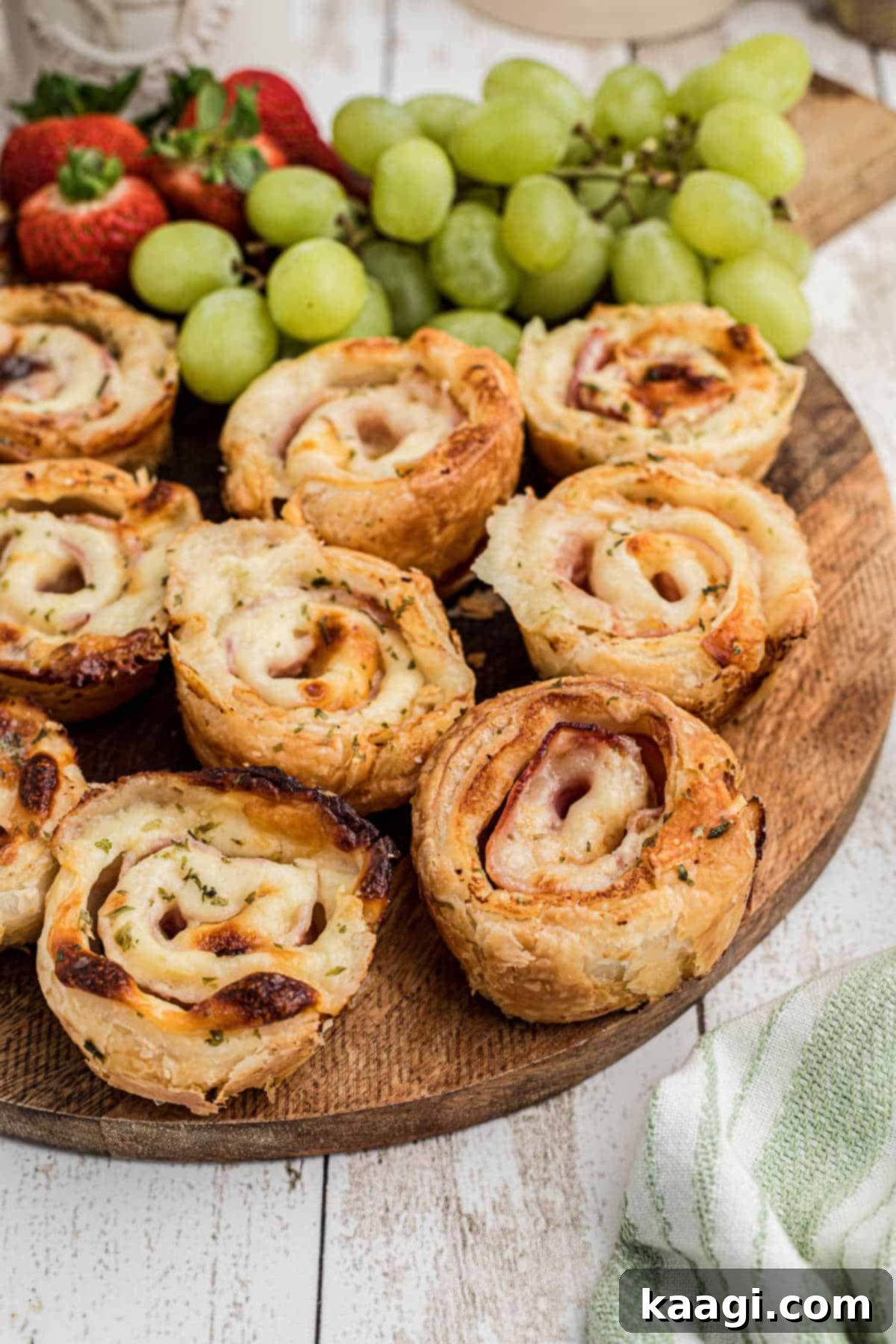 Ham and cheese bites on a board with some fruit in the background.