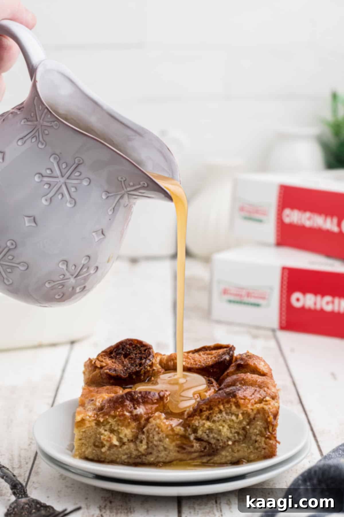 A glorious slice of Krispy Kreme bread pudding resting on a white plate, glistening with a warm vanilla sauce being artfully drizzled over its golden-brown top.