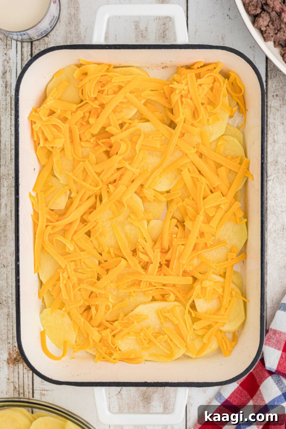 Homestyle Beef and Potato Casserole 7 A generous sprinkling of shredded cheddar cheese covering a layer of sliced potatoes in the baking dish.