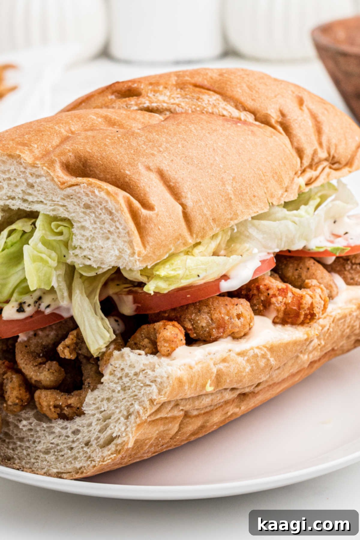 Close up of a bread sub filled with fried crawfish , dressed with lettuce, tomato and mayonnaise.