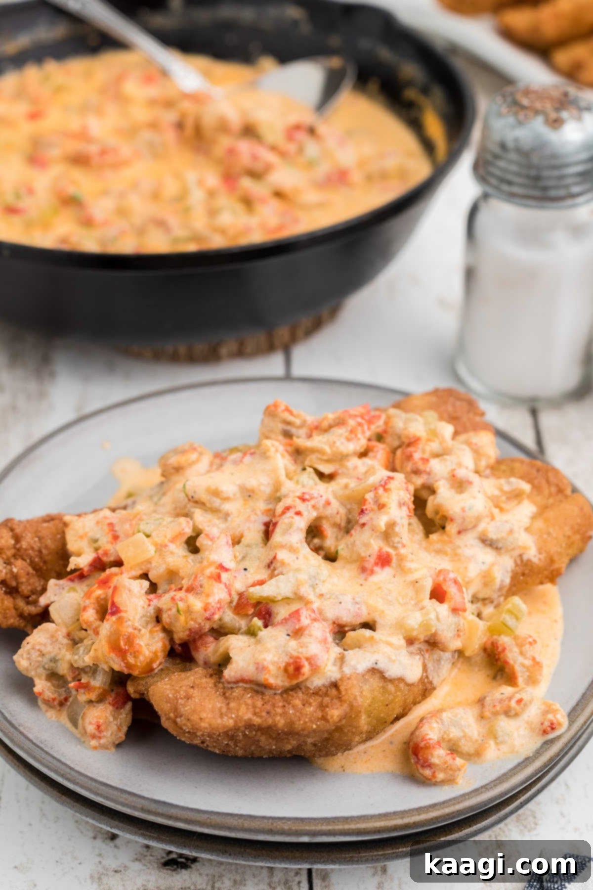 A piece of fried fish with crawfish sauce poured over the top, garnished with fresh herbs, showcasing a delightful meal.