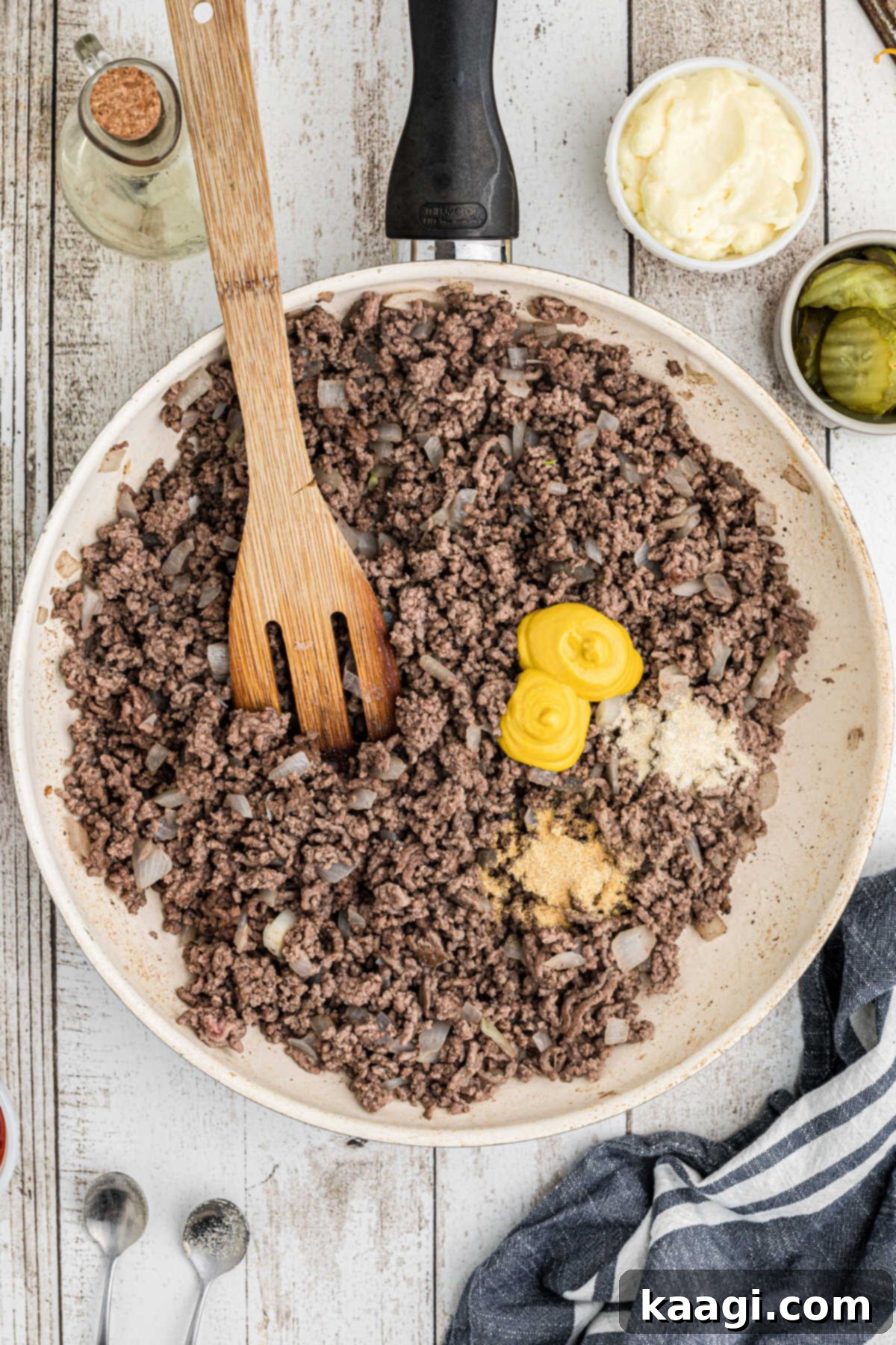 Ultimate Big Mac Comfort Casserole 6 Overhead view of a large skillet filled with cooked ground meat, with some seasoning and mustard on top.