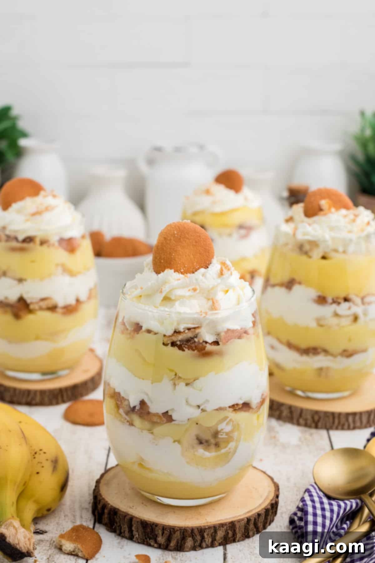 A tall image of some banana pudding cups in elegant glasses, showcasing the layers of creamy pudding, fresh banana slices, and vanilla wafers.