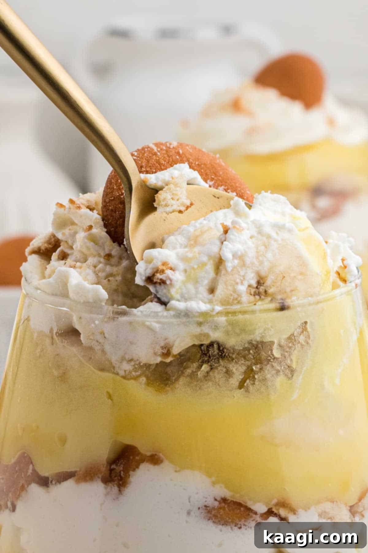 Close up of a banana pudding cup with a spoon taking some out, showing the creamy texture and layers.