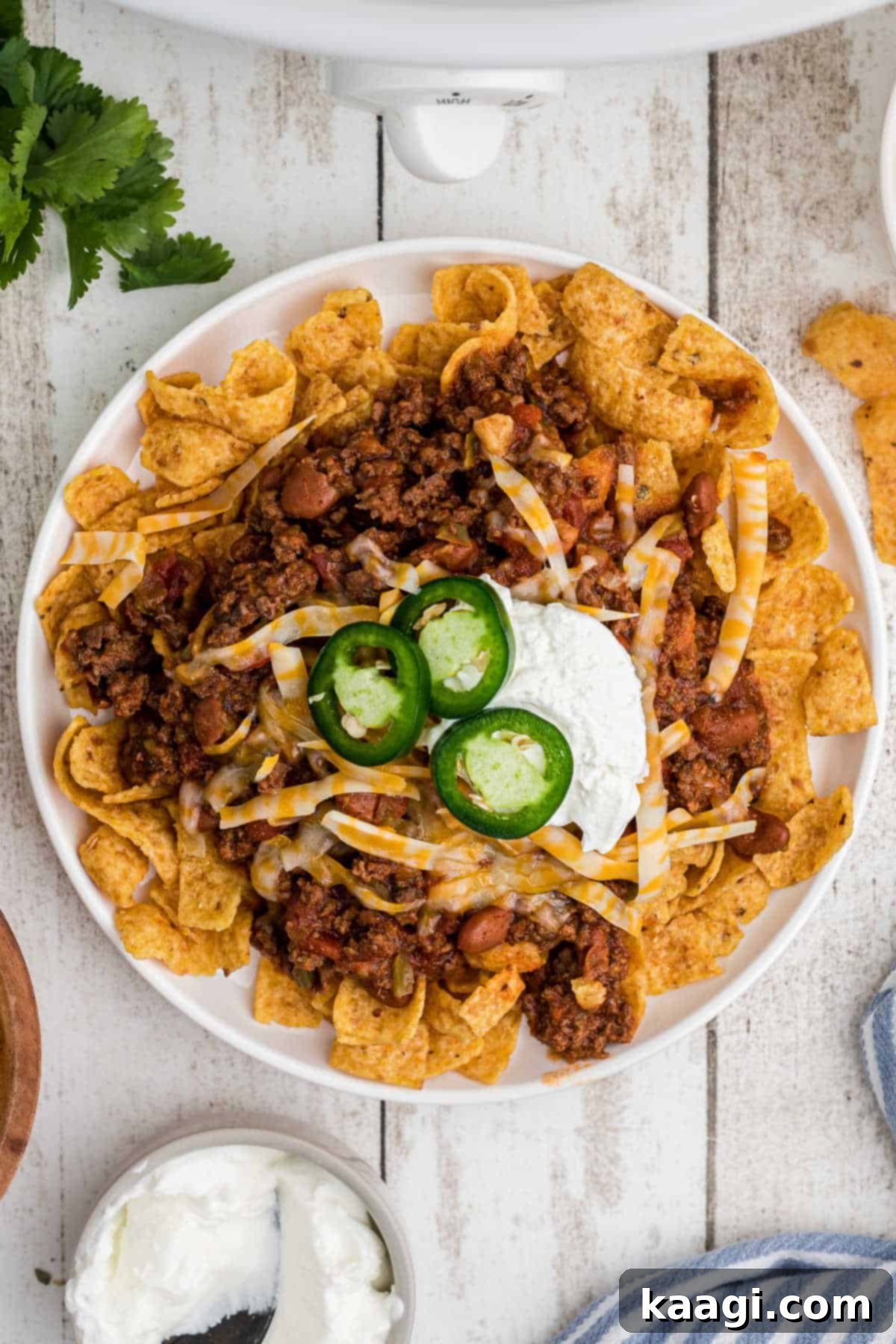 An overhead shot of a plate of crockpot frito pie with some sour cream and cheese, garnished with fresh cilantro.