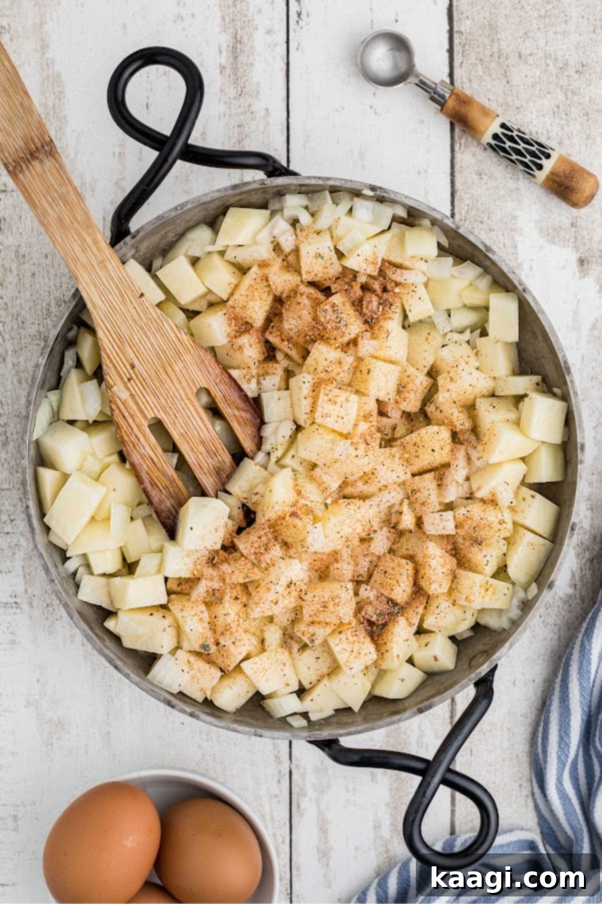 Seasonings being sprinkled over a skillet with cubed potatoes and onions, ready to be stirred and combined.