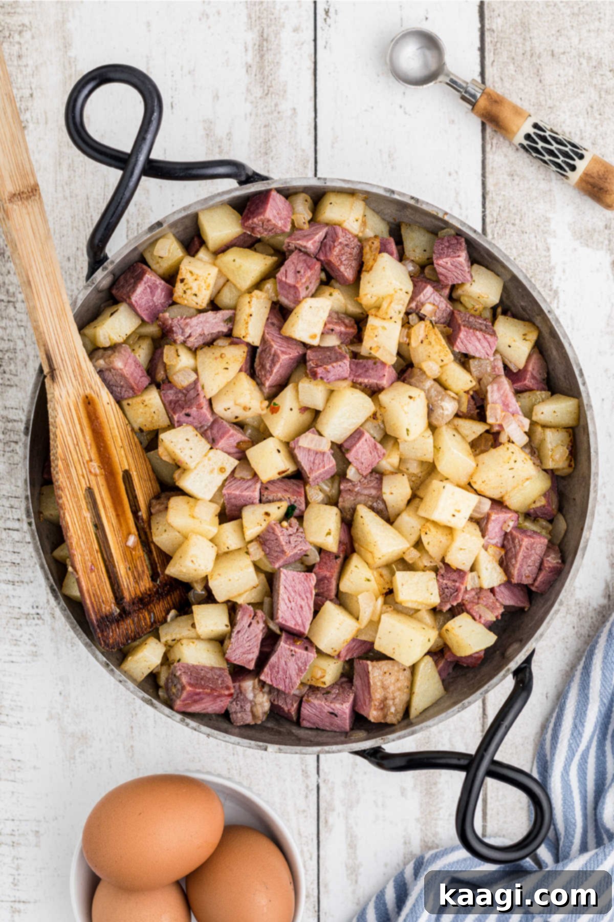 Cooked corned beef, diced into cubes, added to the skillet with the seasoned potatoes and onions, ready for further cooking.