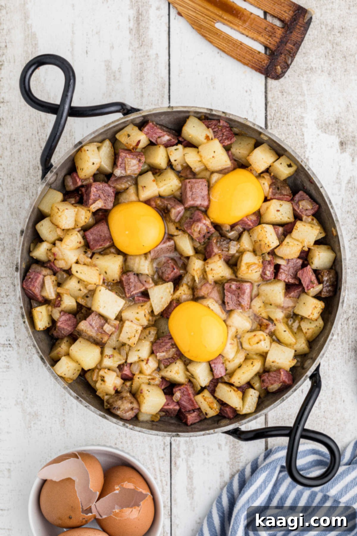 A large skillet with the finished corned beef hash, topped with three freshly cracked eggs, before being placed in the oven.