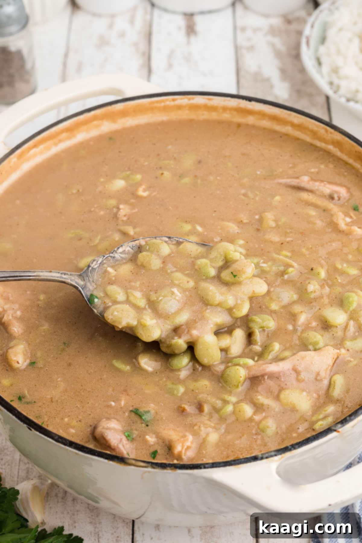 A spoon digging into a pot of chicken and lima beans, showing the rich gravy.