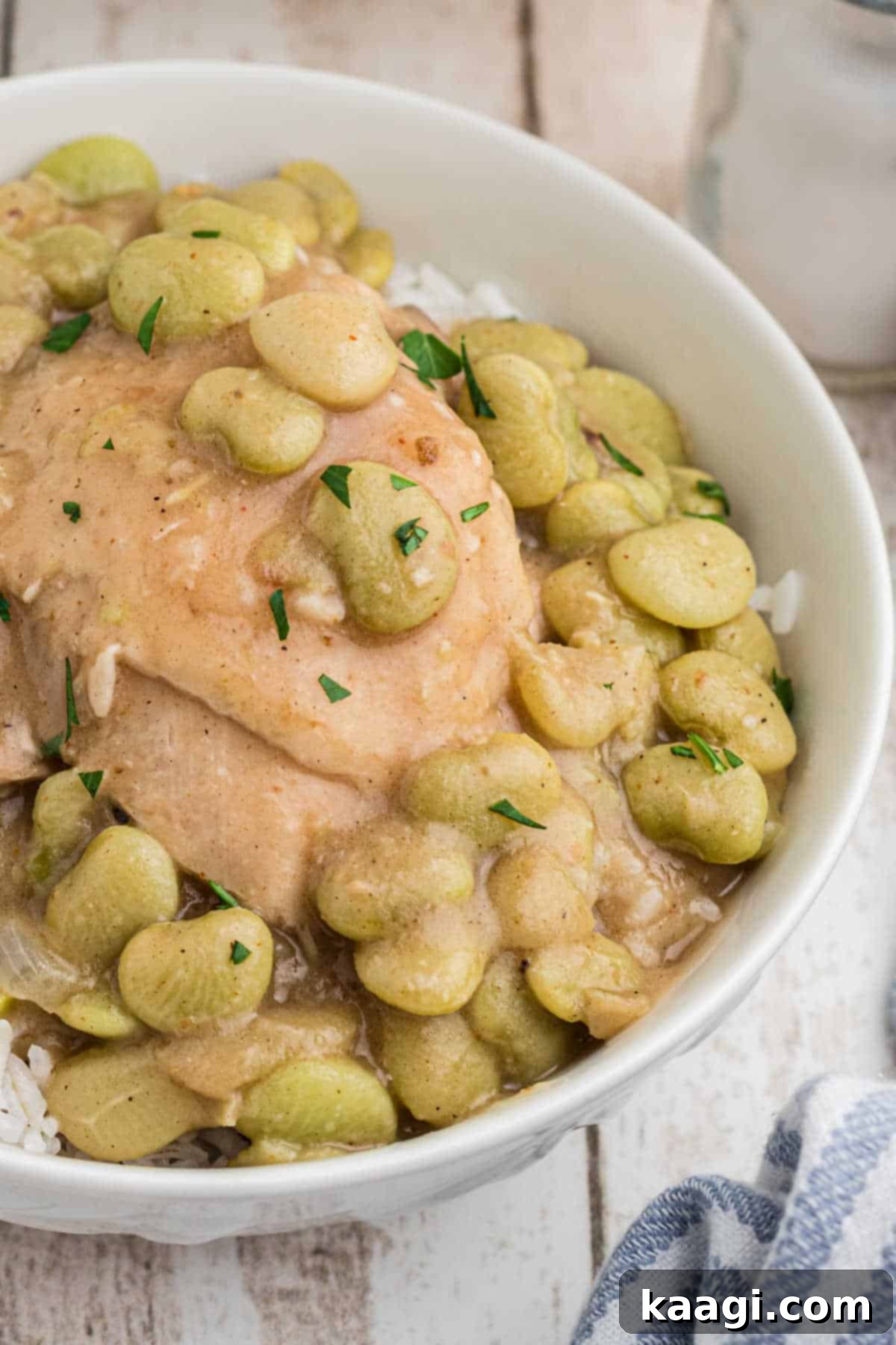 Close up of a bowl of chicken and lima beans on rice, garnished with parsley.