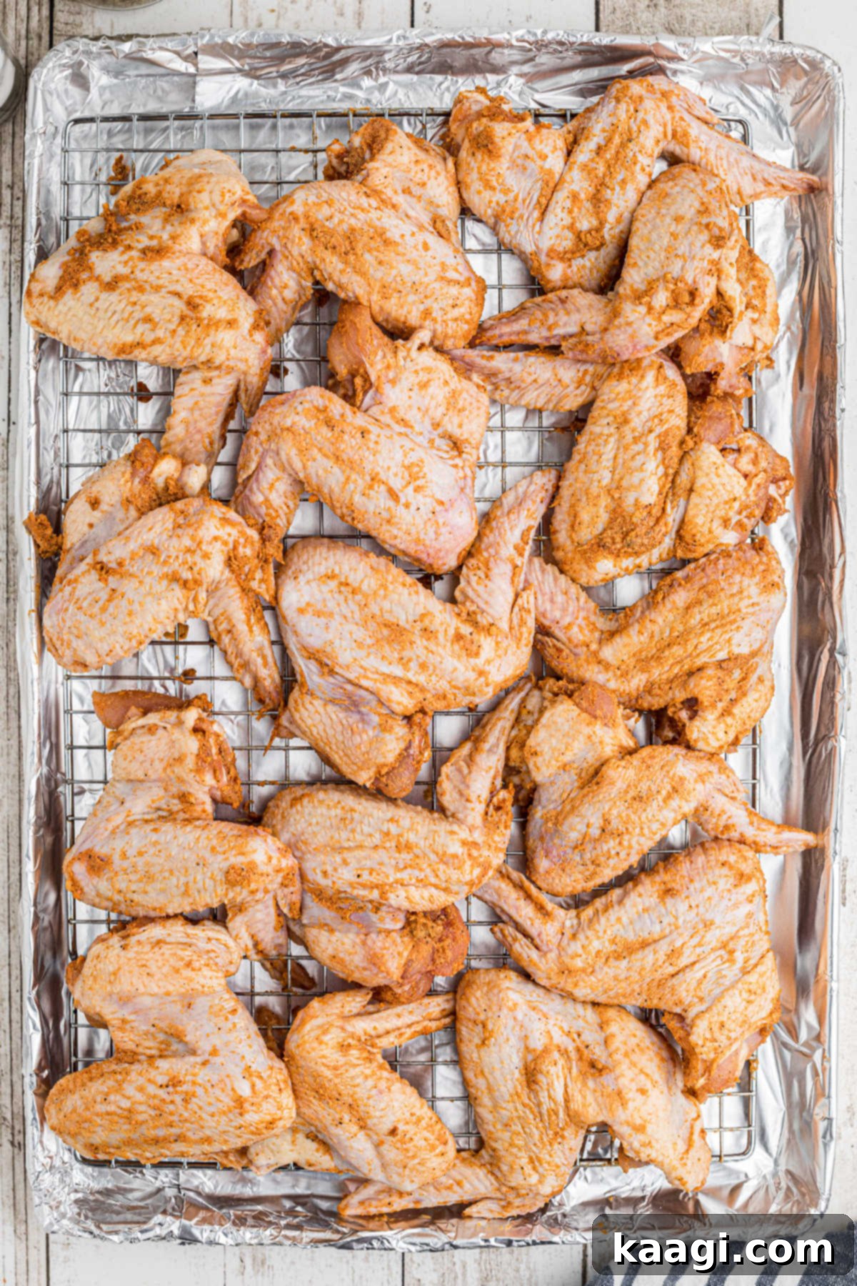 Homemade Wingstop Louisiana Rub 7 Seasoned chicken wings arranged neatly on a wire rack set on a baking sheet, ready for the oven.