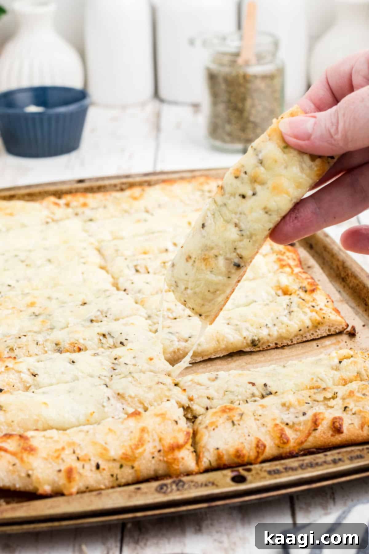 Someone lifting a golden-brown piece of Italian Cheese Bread off of a baking sheet, showcasing its melted cheese and crispy crust.