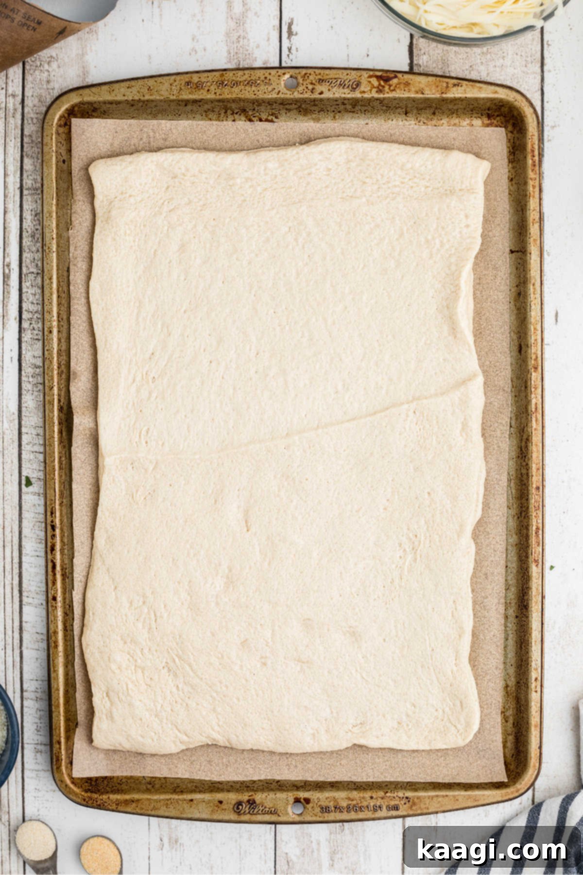 An unrolled, ready-made pizza crust meticulously laid out on a baking sheet lined with parchment paper, preparing for the next steps.
