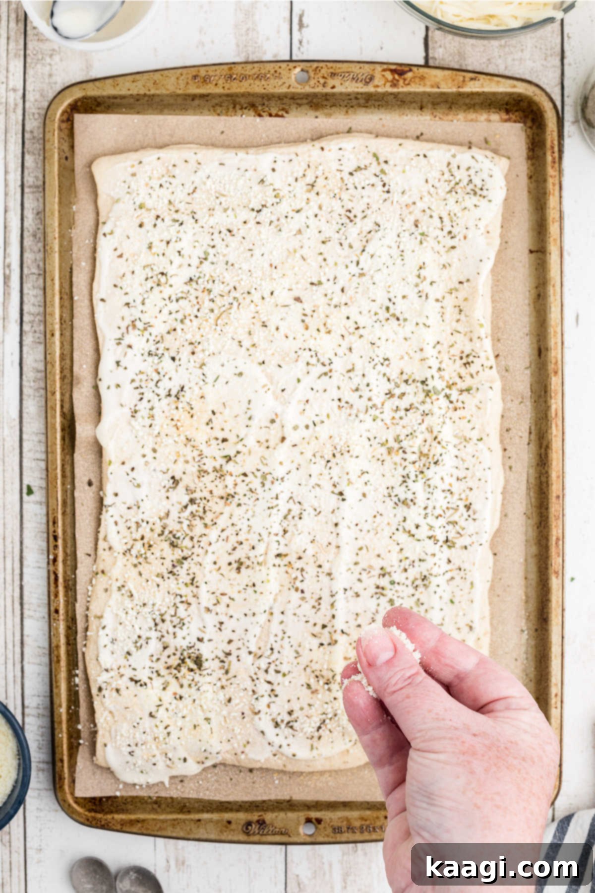 Various seasonings and grated Parmesan cheese being sprinkled generously over the ranch-dressed pizza crust, adding layers of flavor.