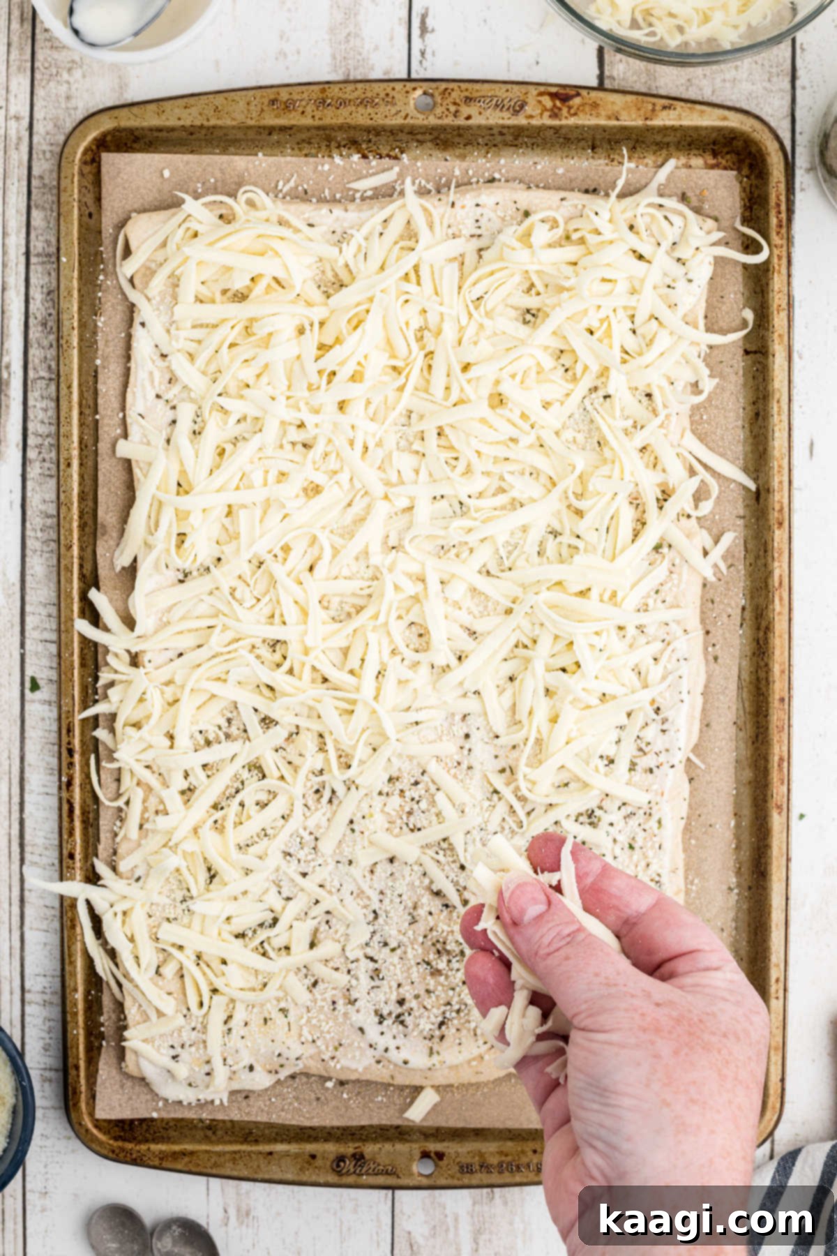 Shredded mozzarella cheese being lavishly spread on top of the seasoned and Parmesan-covered pizza crust, ready for baking.