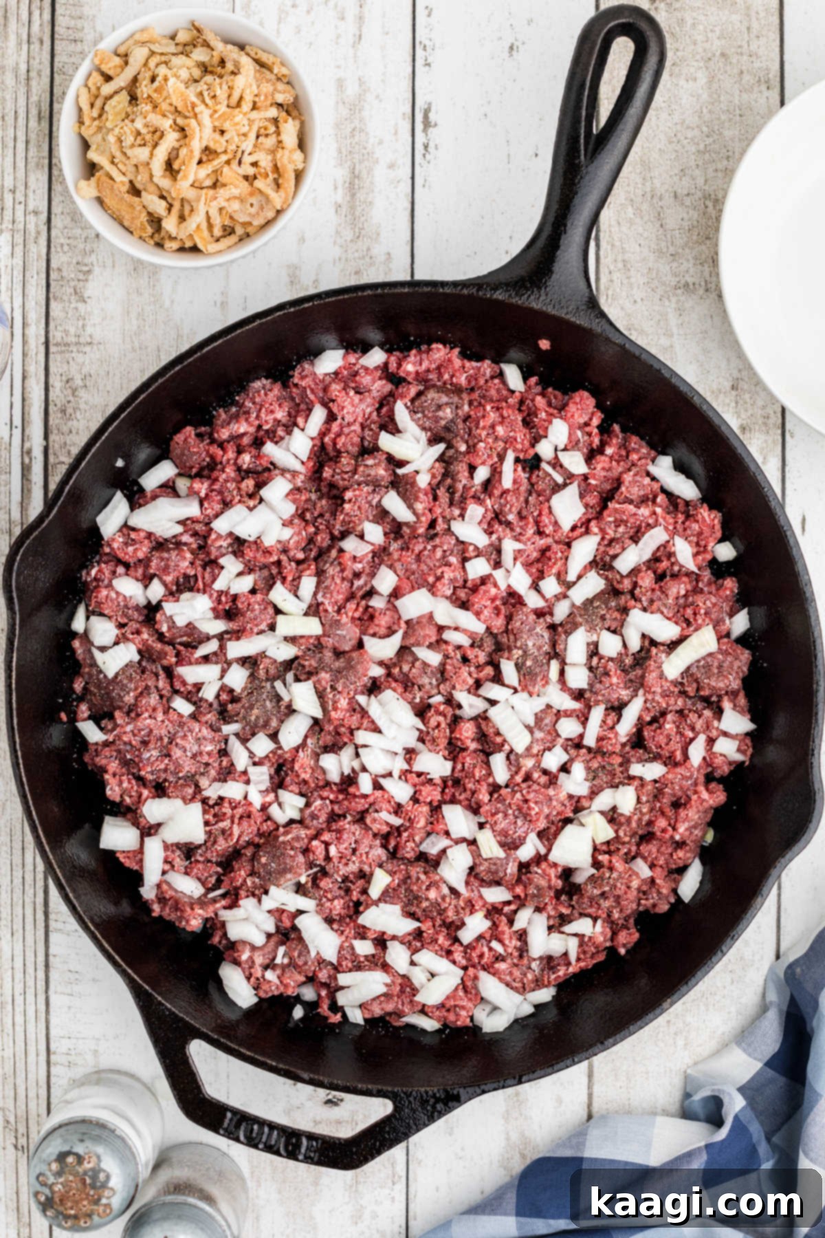 Overhead image of a cast iron skillet with ground beef topped with diced onions.