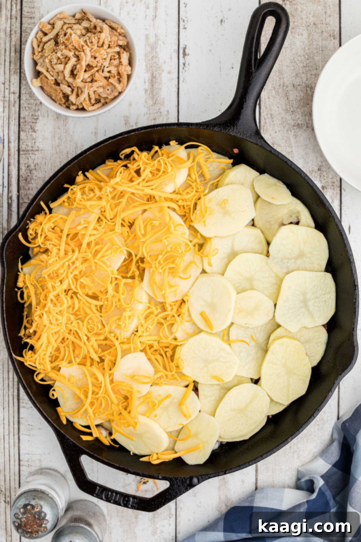 Overhead image of a cast iron skillet with potatoes and grated cheese sprinkled on top.