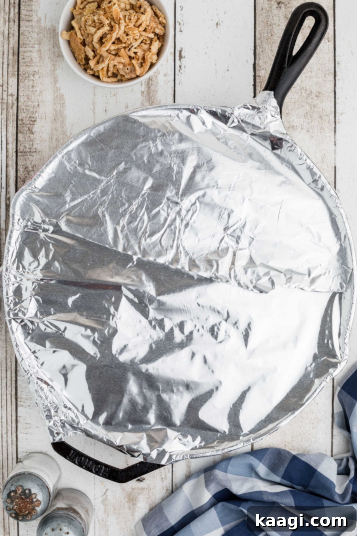 Overhead view of a black skillet covered with aluminum foil, ready for baking.