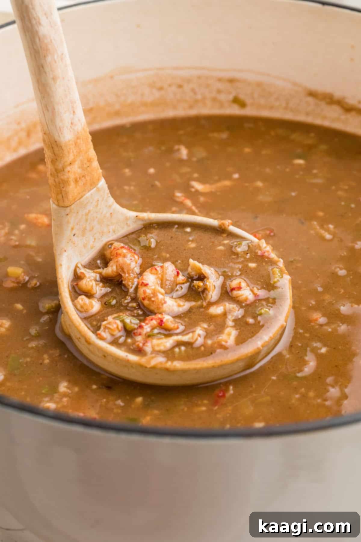 A large pot filled with bubbling crawfish stew, with a ladle poised to scoop out a serving.