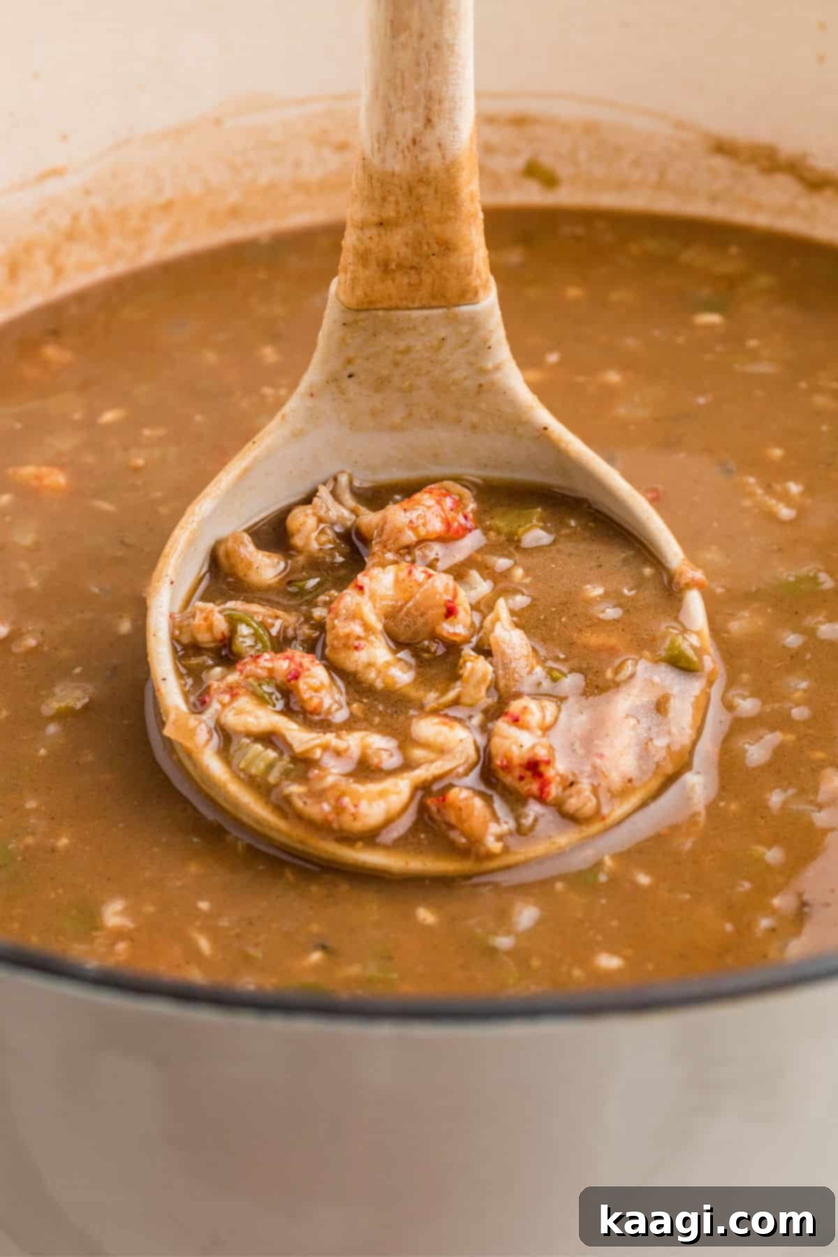 A ladle scooping a generous portion of rich, savory crawfish stew from a pot, highlighting its vibrant color and tender crawfish pieces.