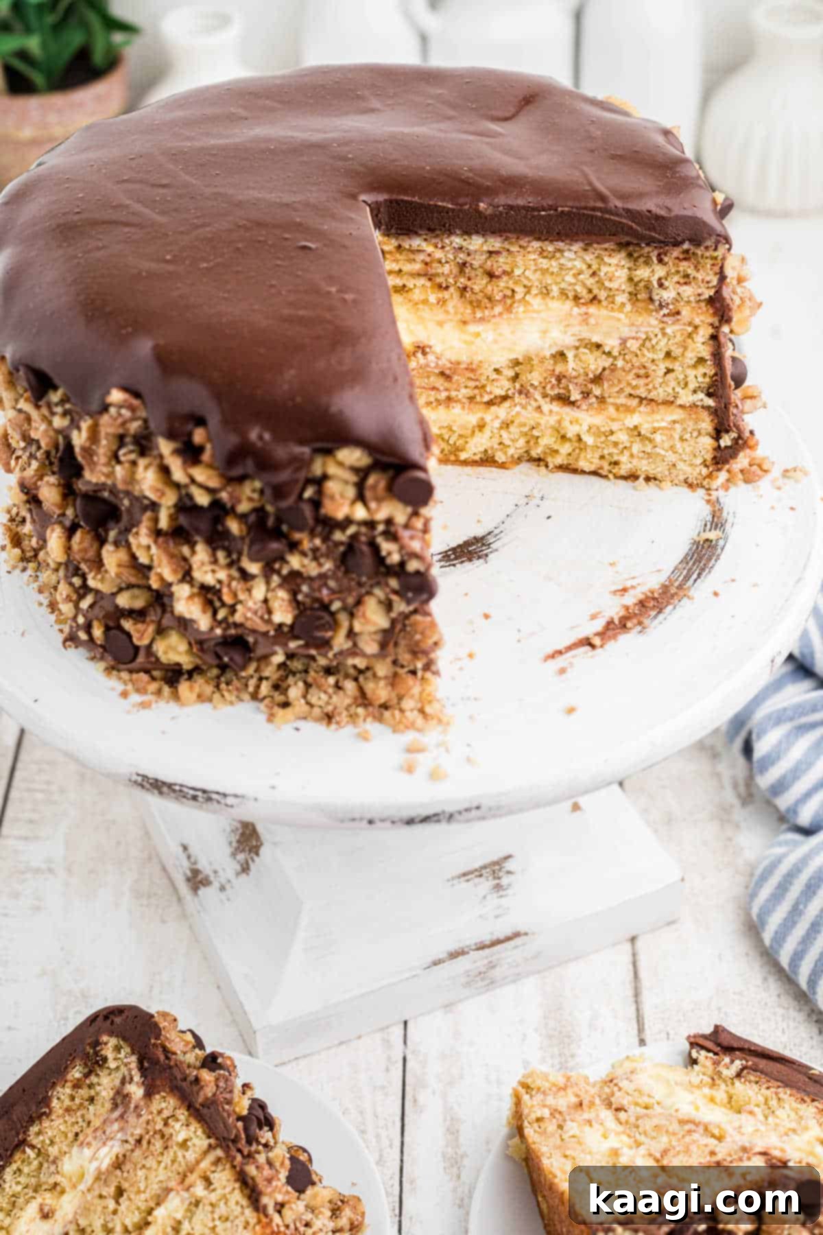 A fully assembled Banana Dream Cake with a slice already removed, showcasing its layers of banana cake, cream filling, and chocolate ganache.