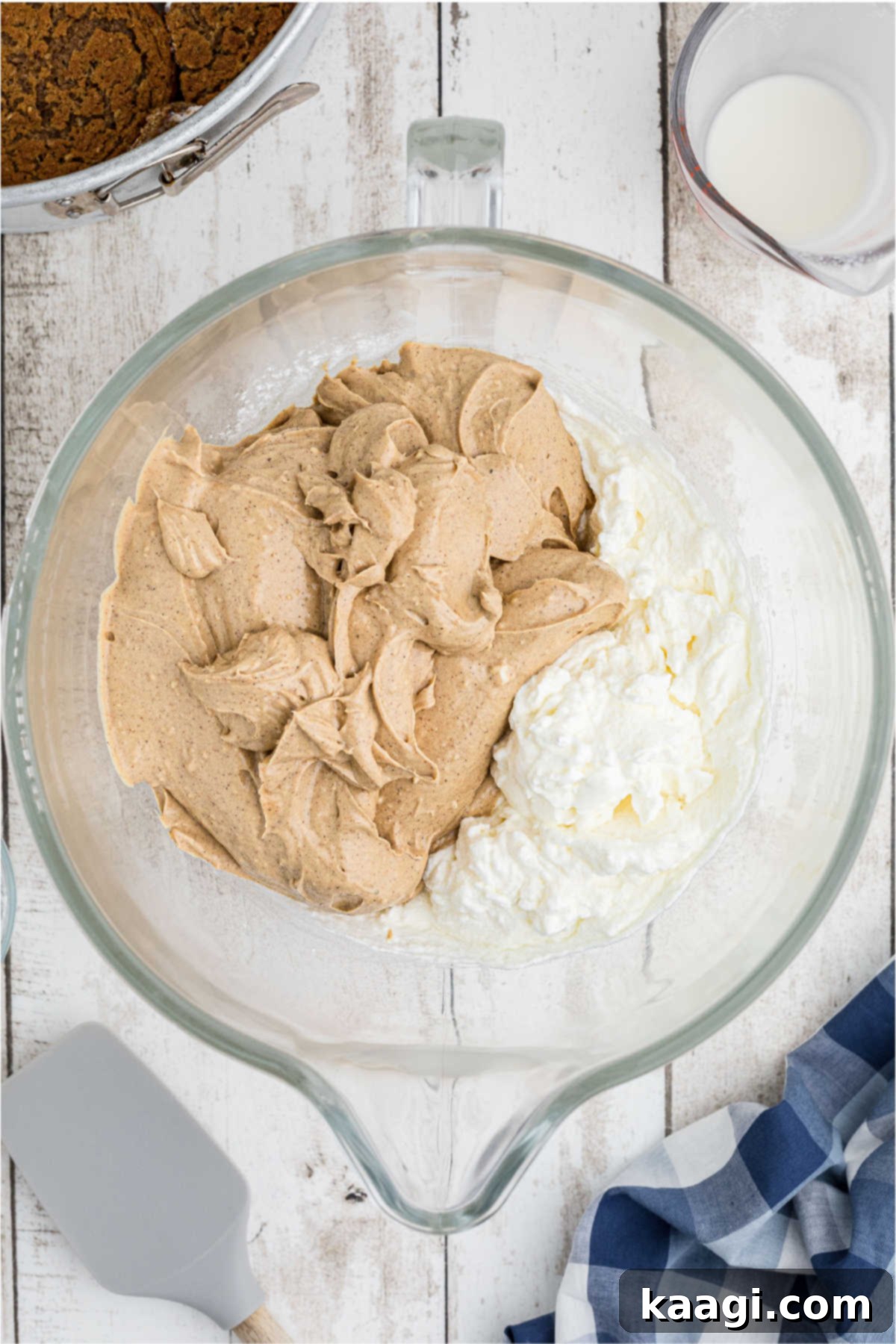 Cream cheese mixture being gently folded into whipped cream in a large mixing bowl.