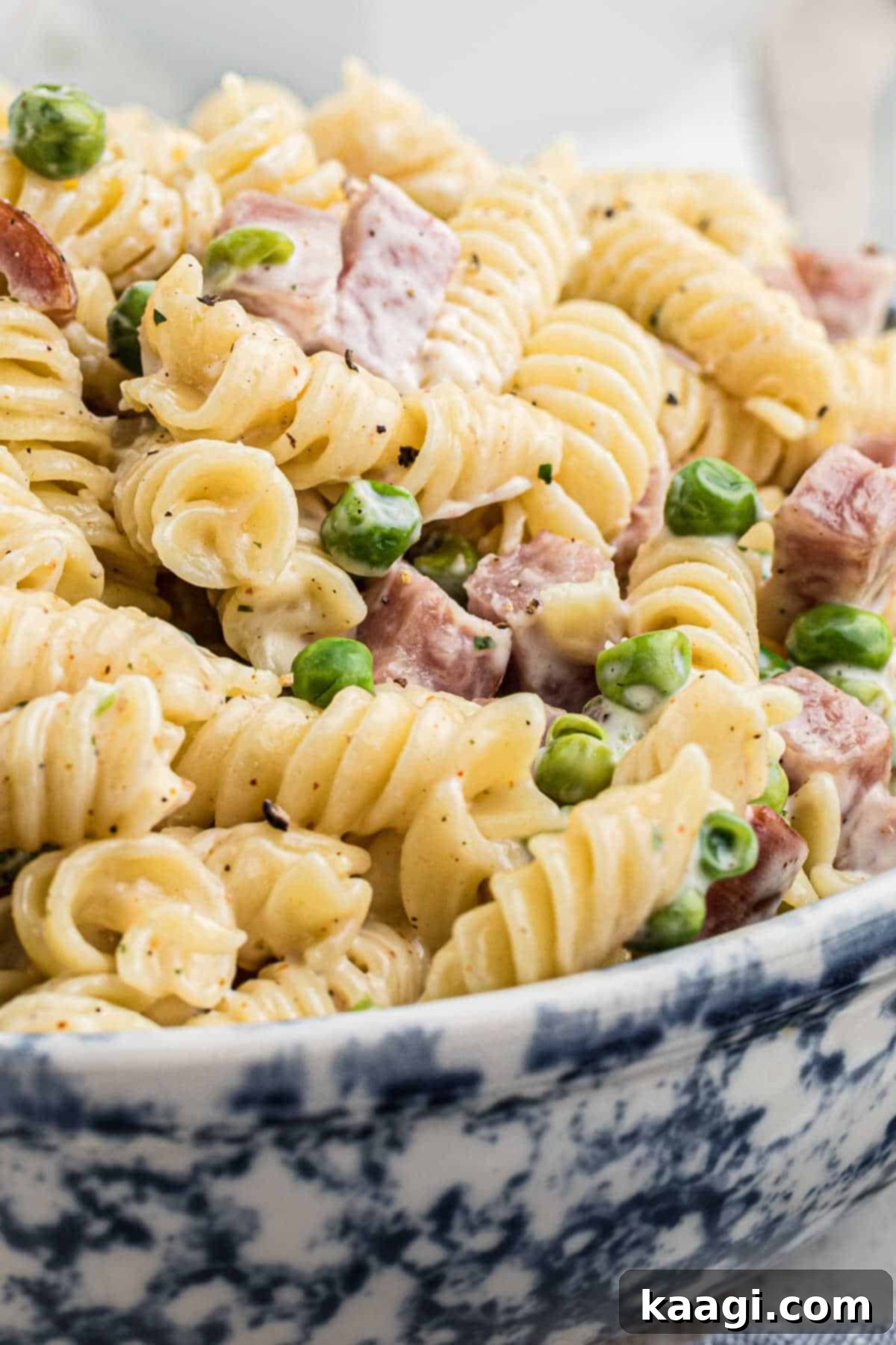 Very close up side shot of a bowl of Ruby Tuesday ham and pea pasta salad, showcasing its creamy texture and fresh ingredients.