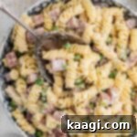 Close up of a bowl of Ruby Tuesday ham and pea pasta salad with a spoon digging in, showing the creamy texture.