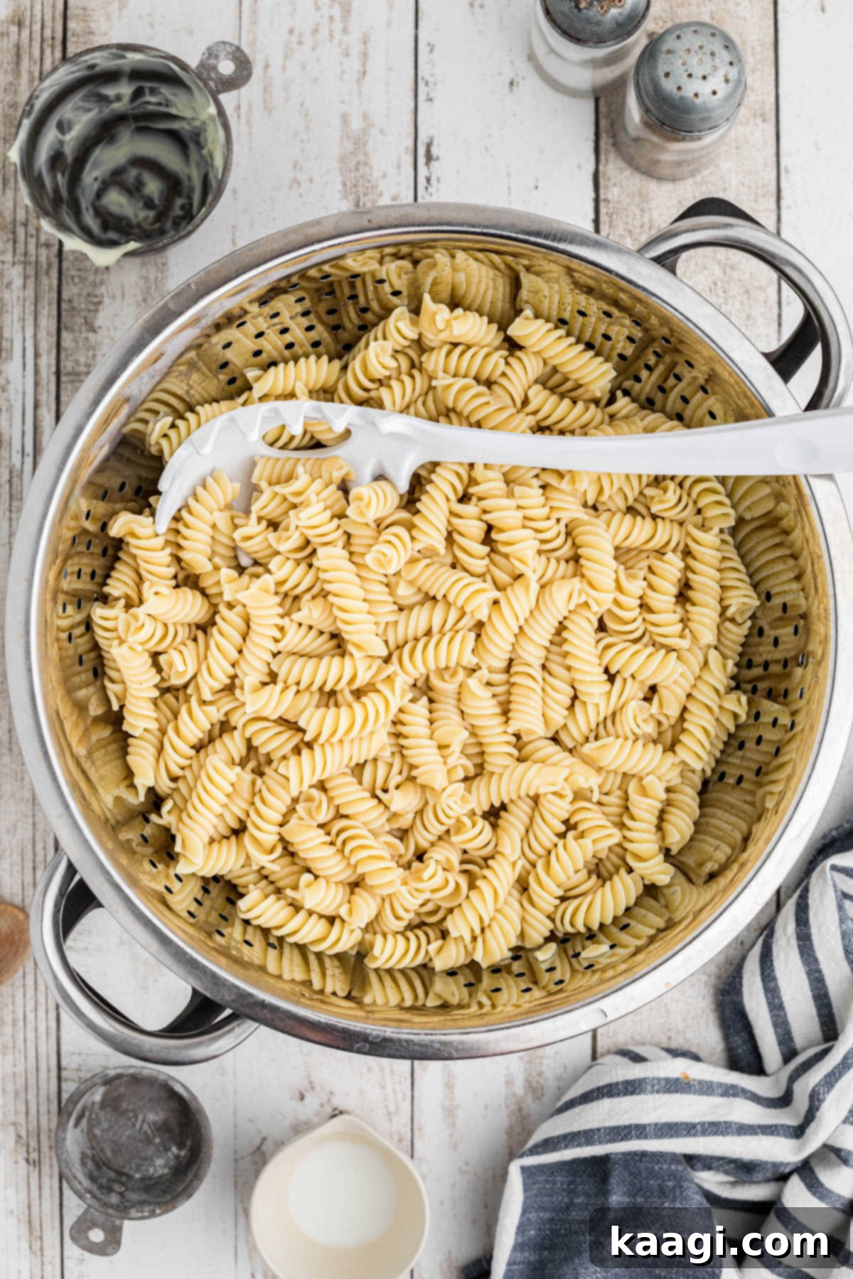 Cooked rotini pasta in a colander, with a pasta fork, after being rinsed and cooled.