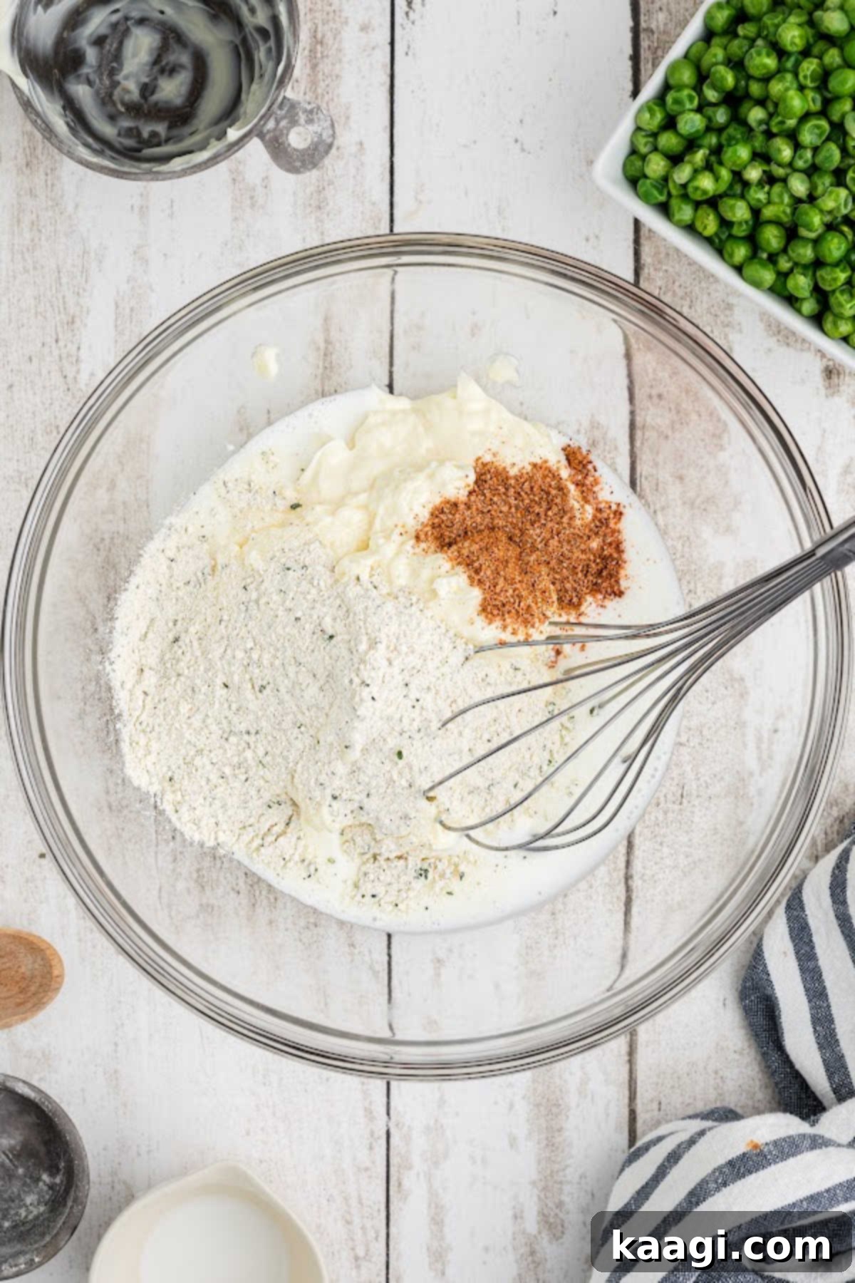 A large mixing bowl containing mayonnaise, buttermilk, ranch dressing mix, and seasoning, ready to be whisked.