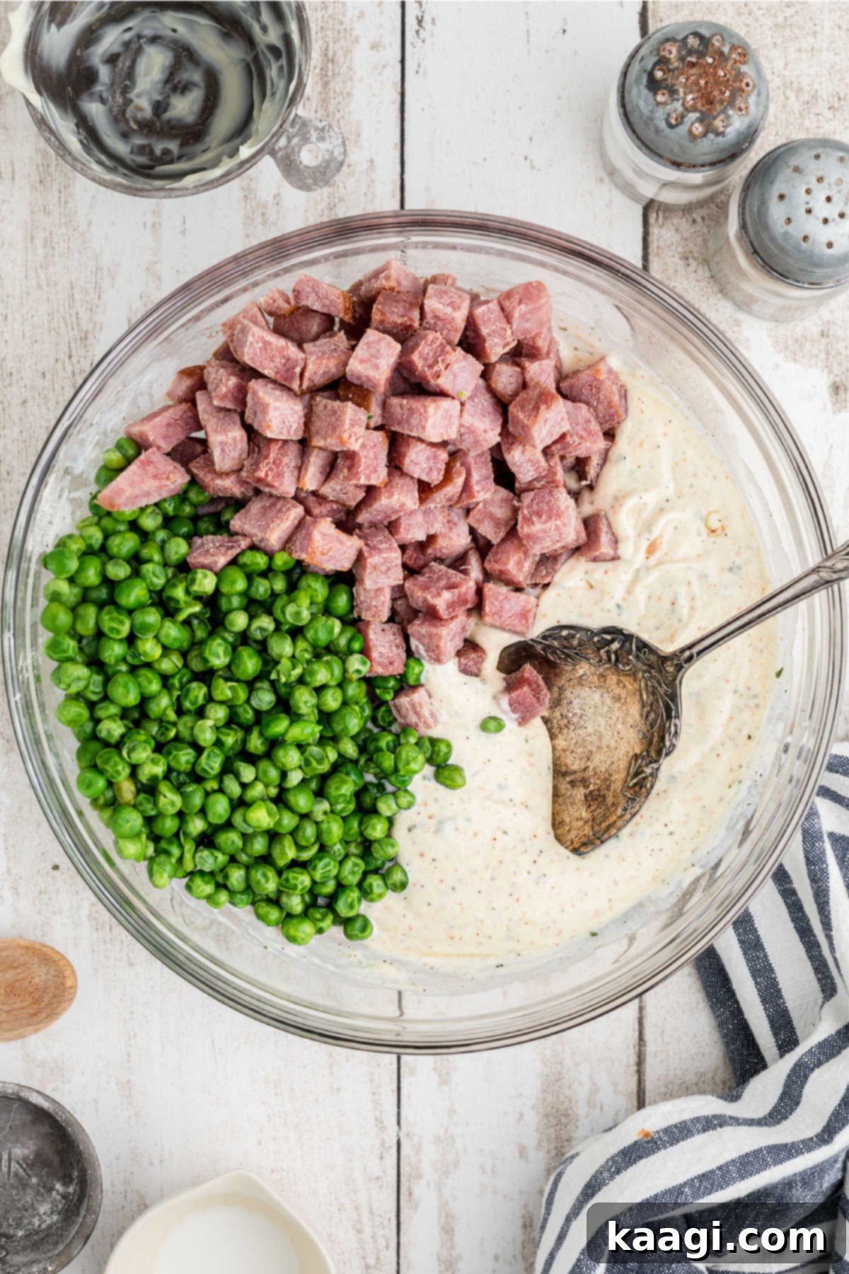 A large mixing bowl containing the creamy dressing with chopped ham and thawed peas, about to be mixed together.
