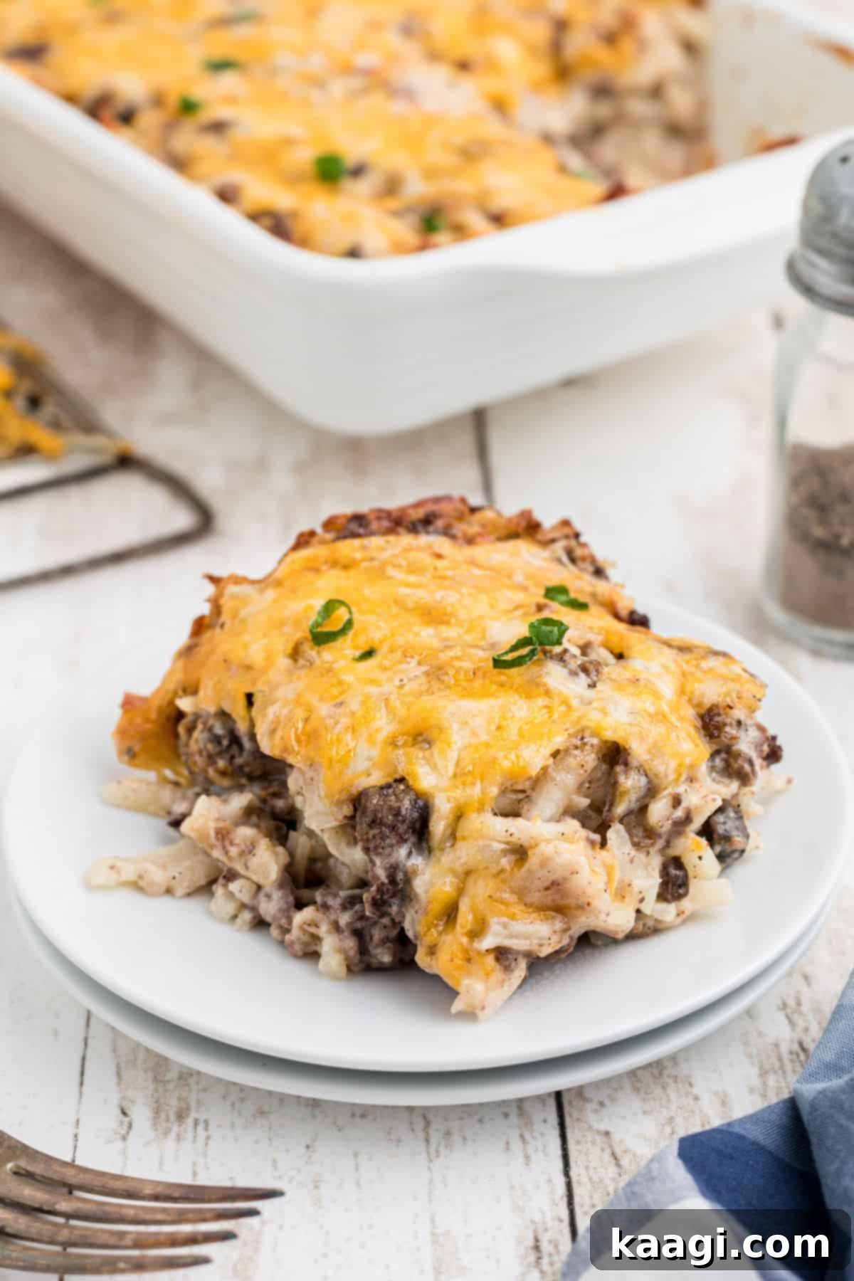 A plate of Hamburger Hashbrown Casserole served, with the casserole dish visible in the background.