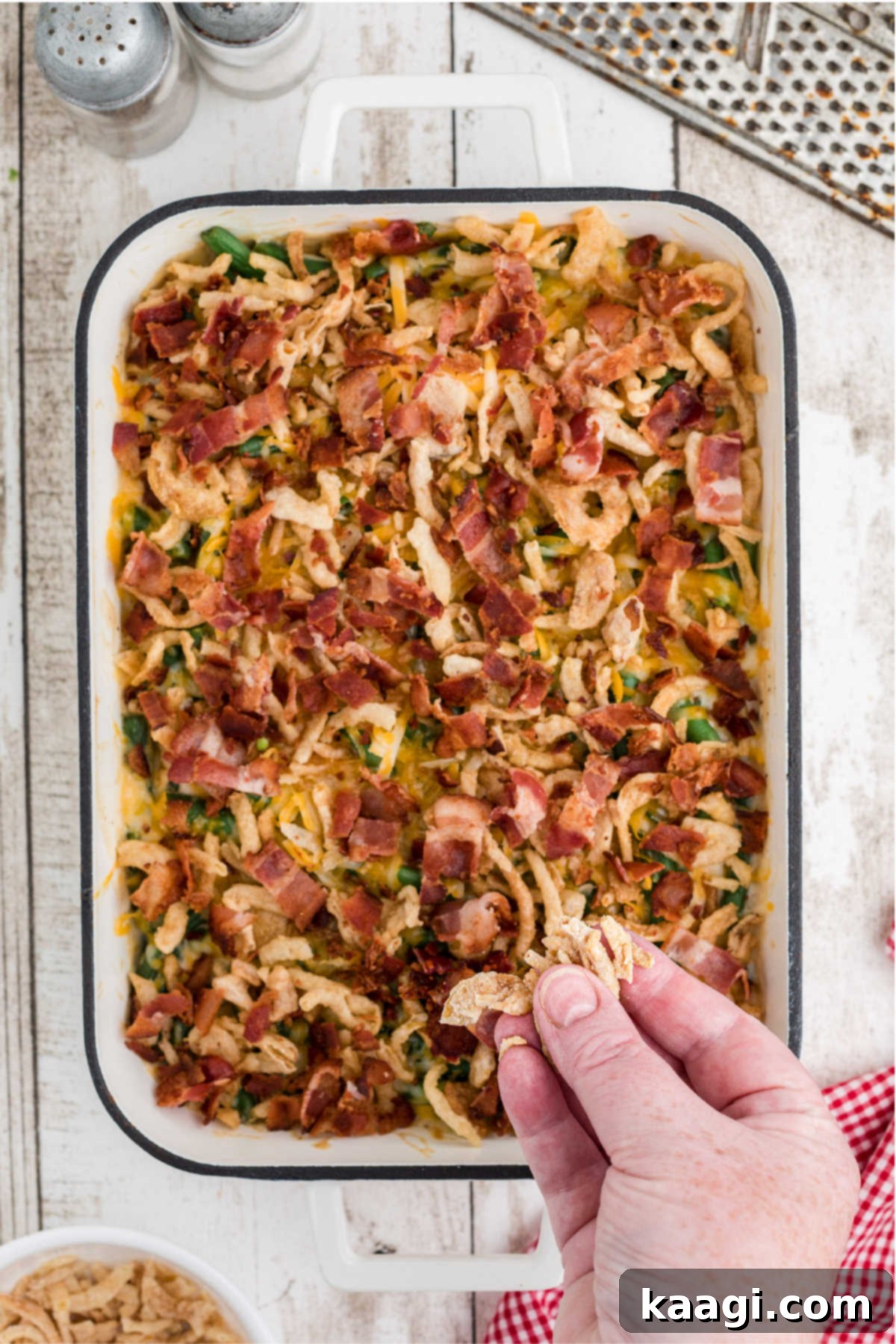 Fried onions being sprinkled on top of a green bean casserole.