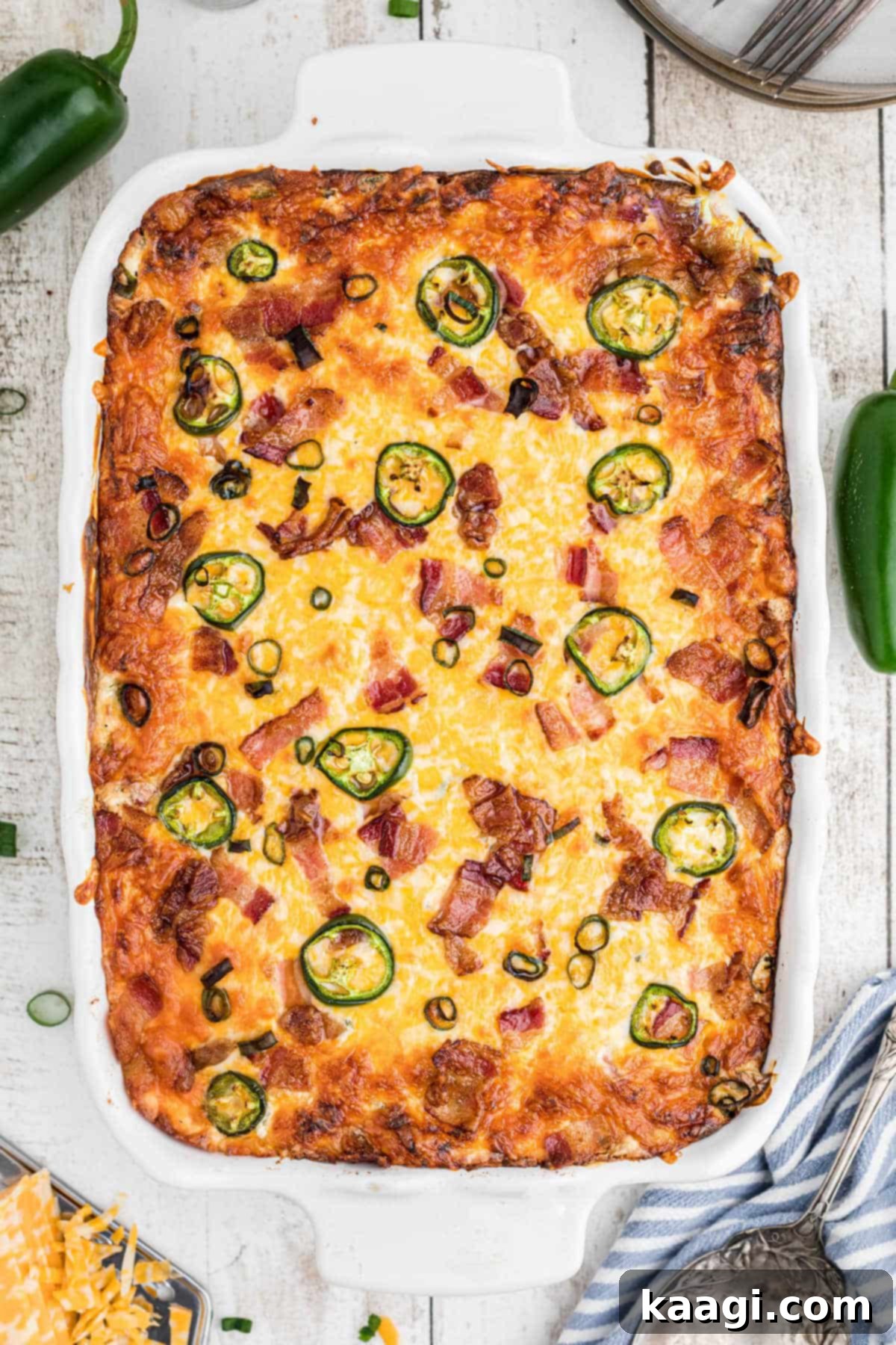 An inviting overhead shot of a bubbly, golden-brown casserole dish filled with Jalapeno Popper Tater Tot Casserole, garnished with fresh green onions and crispy bacon bits.