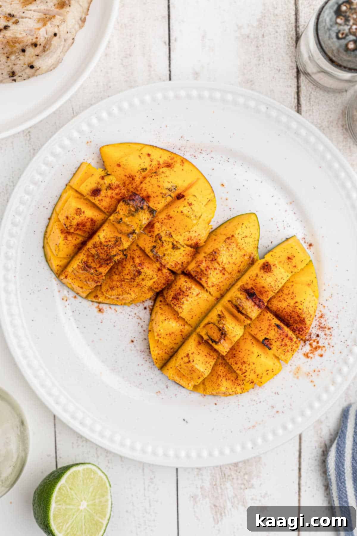 Two vibrant halves of grilled mango, artfully arranged on a clean white plate, showcasing their inviting golden-brown char and succulent flesh.