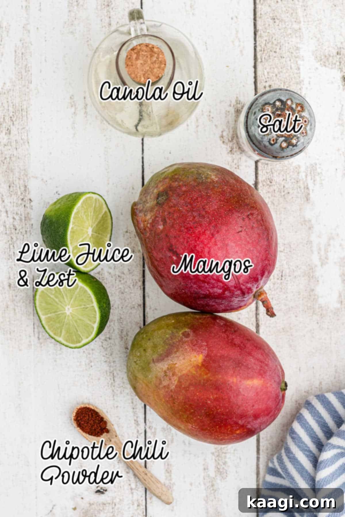 Essential ingredients for grilled mango recipe laid out on a wooden surface, including fresh mangoes, lime, oil, salt, and chili powder.