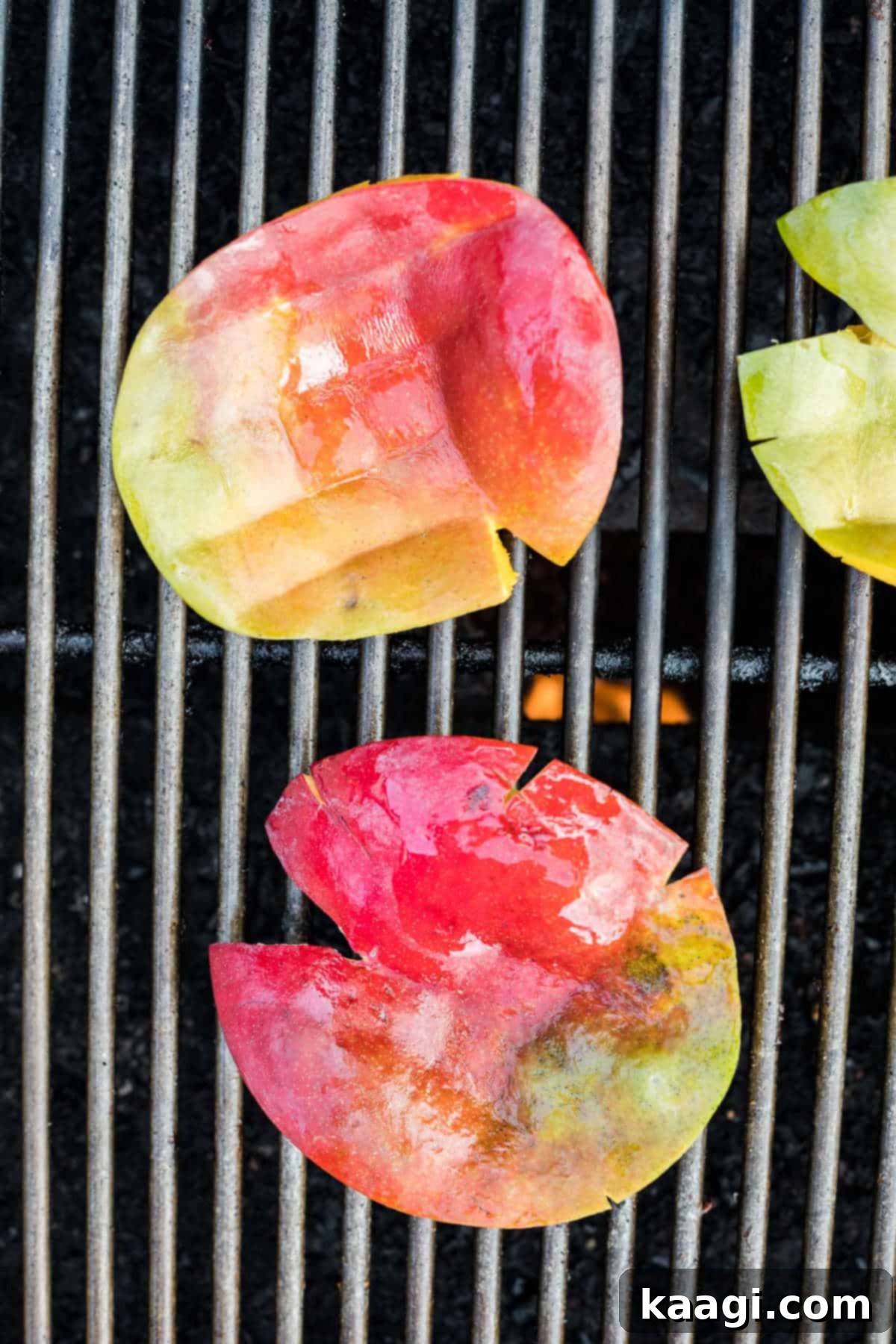 Two halves of mango with scored flesh being grilled on a barbecue grate.