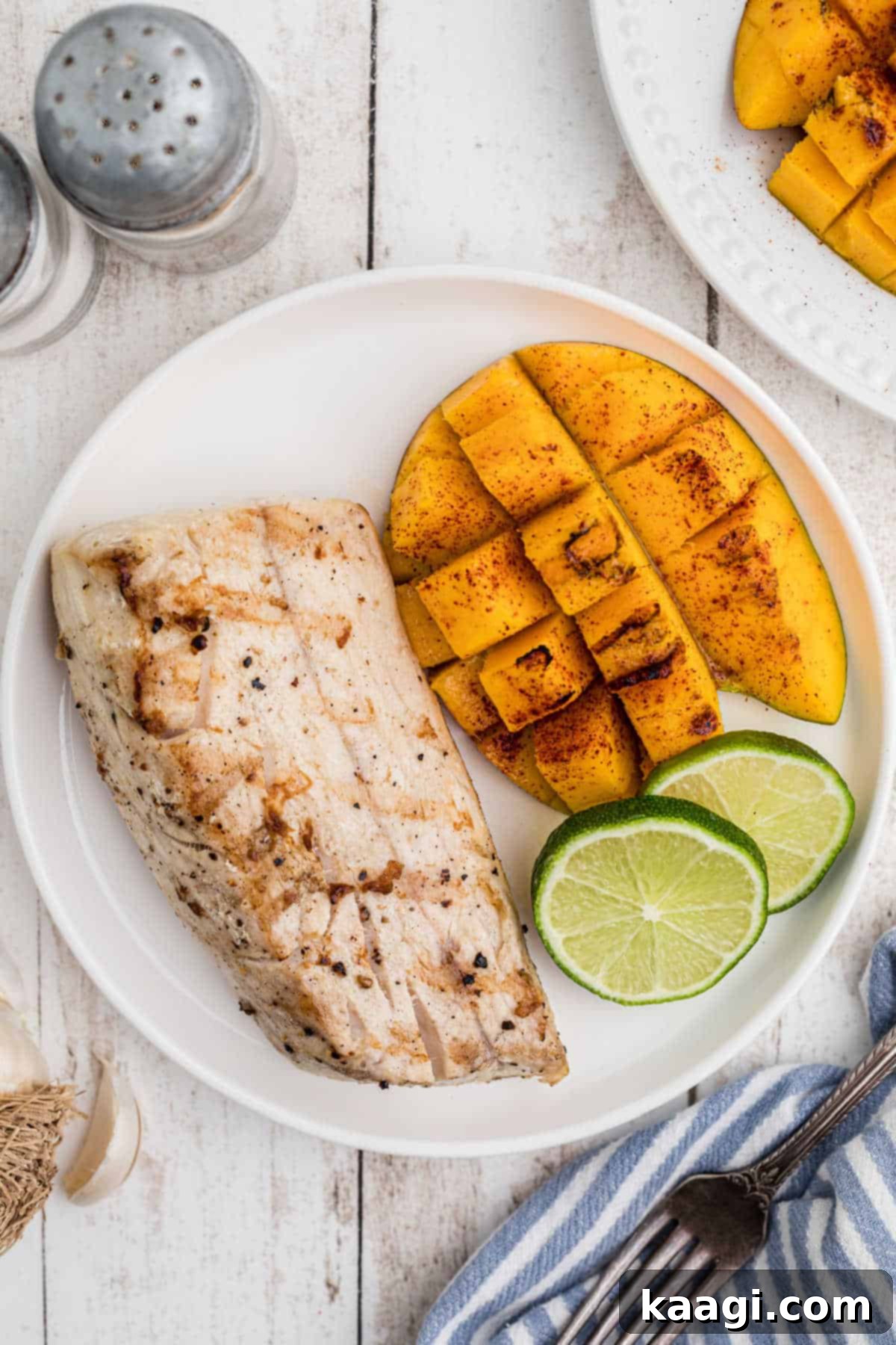 A vibrant plate featuring a piece of perfectly grilled mango alongside a flaky, grilled cobia fillet, garnished with fresh herbs.